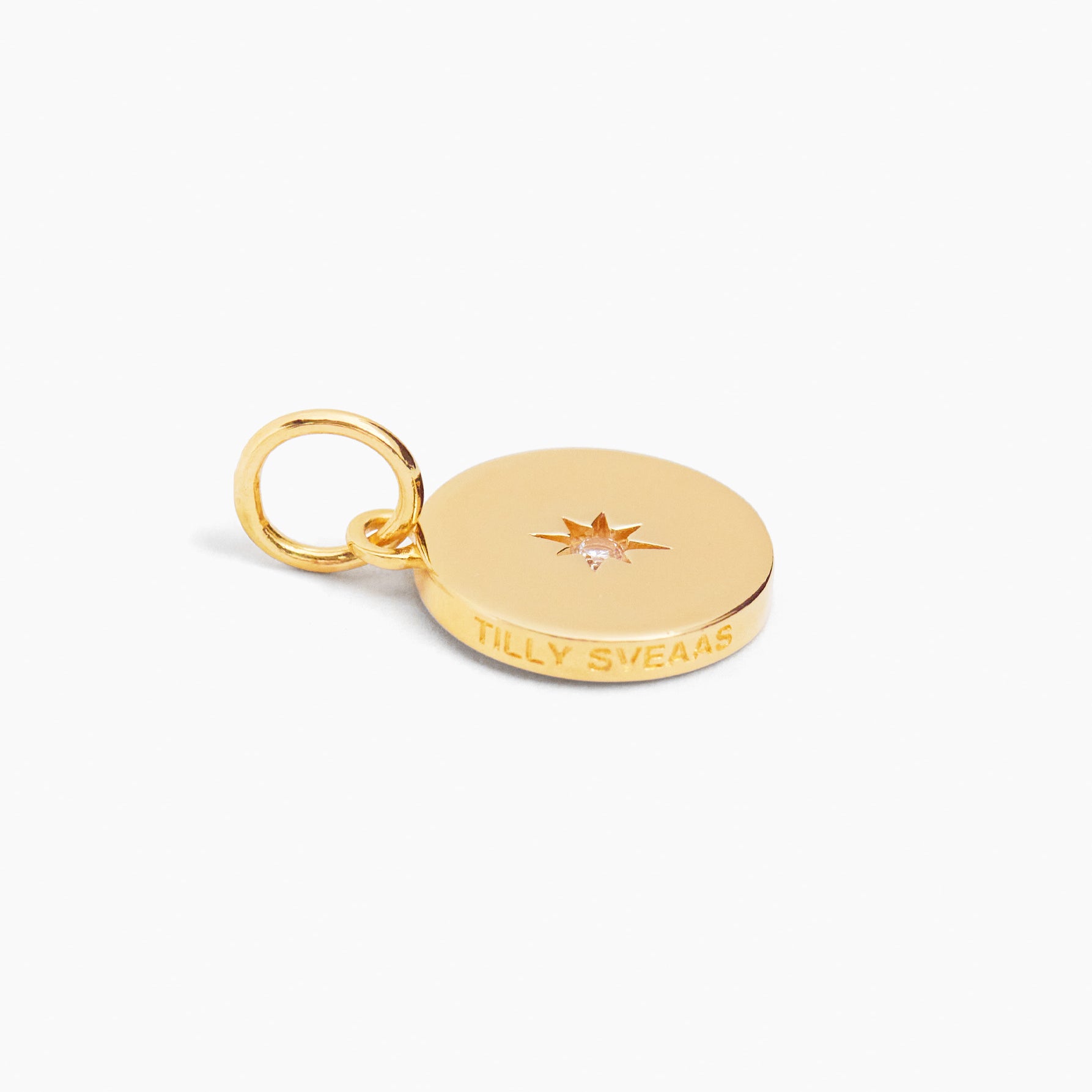 Gold disc charm with ring loop, small starburst gem, and engraved lettering.