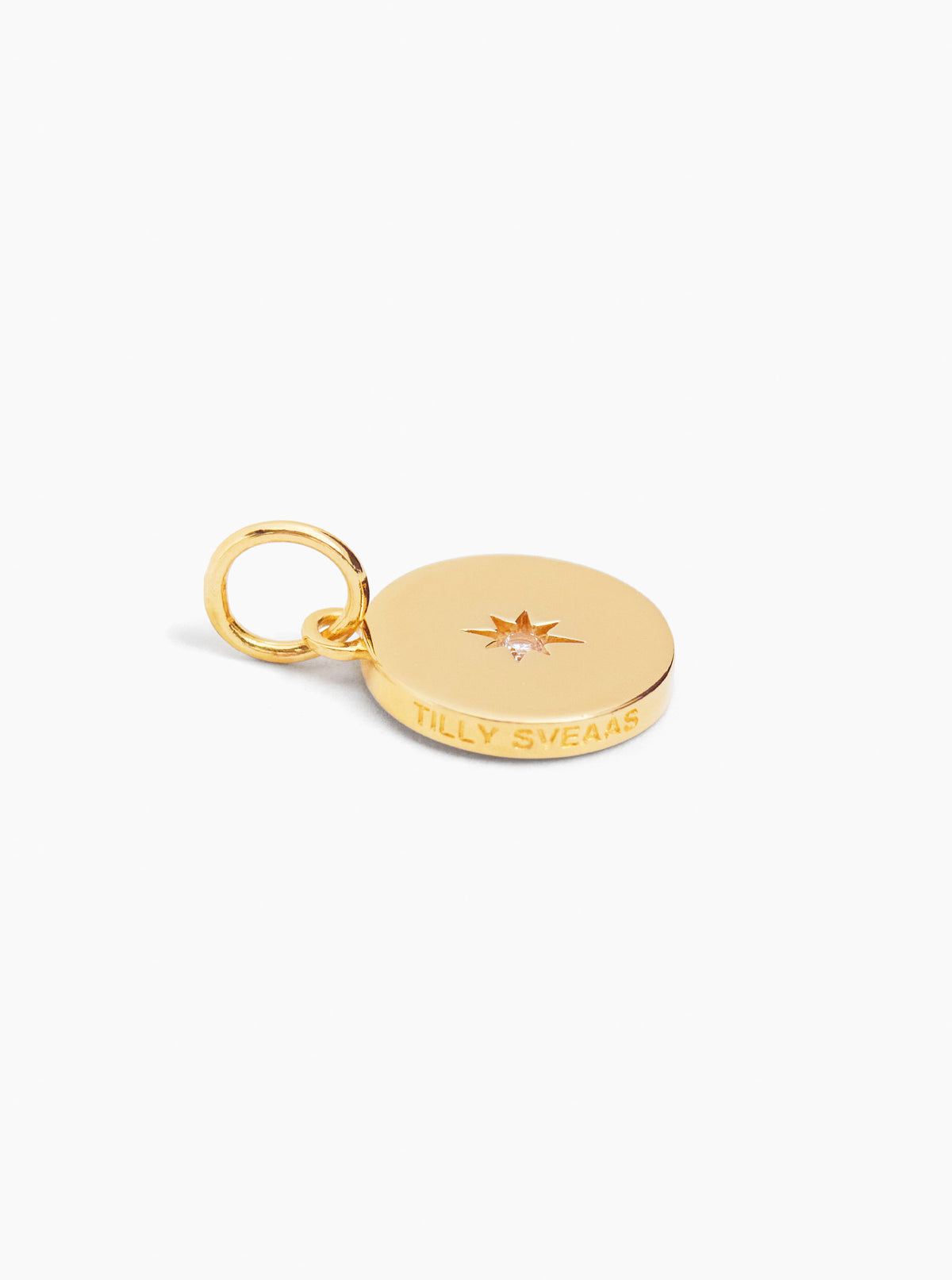 Gold disc charm with ring loop, small starburst gem, and engraved lettering.