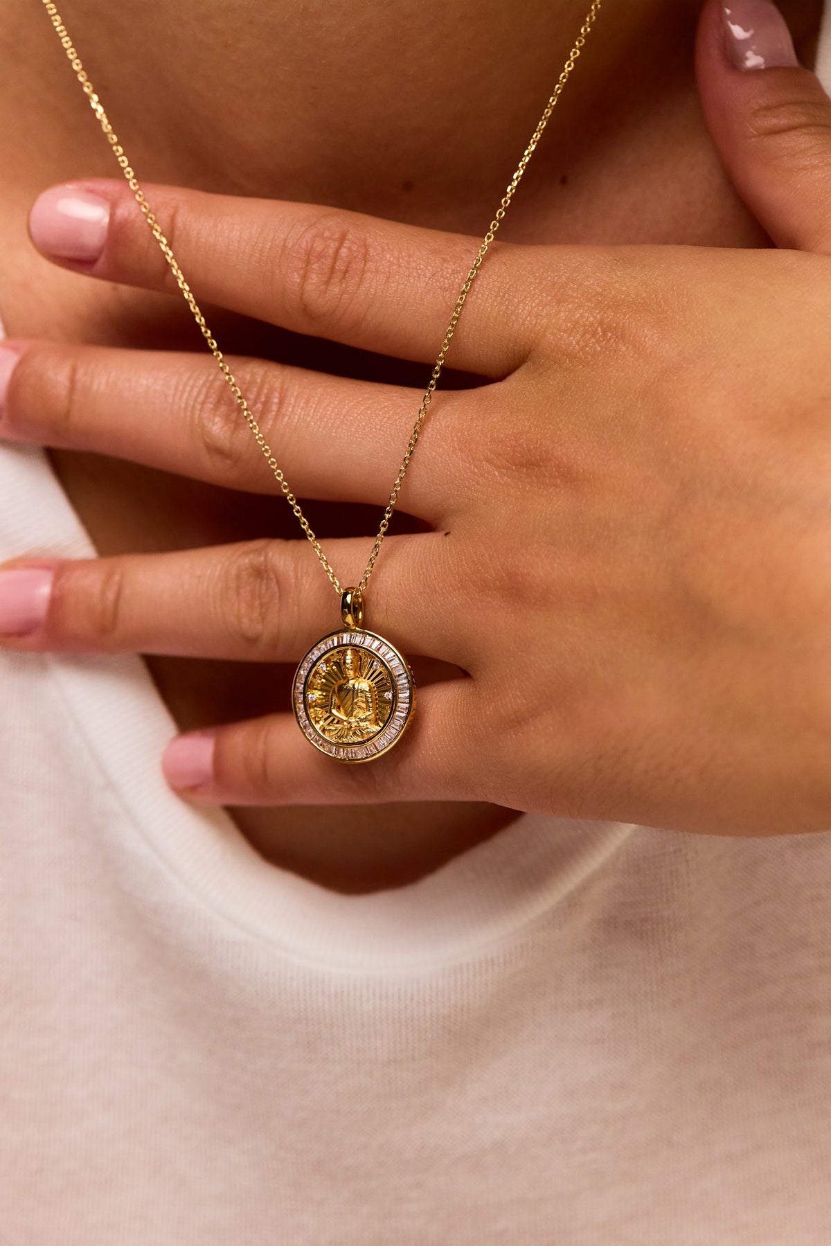Gold trace chain necklace with round Buddha medallion pendant, held in hands