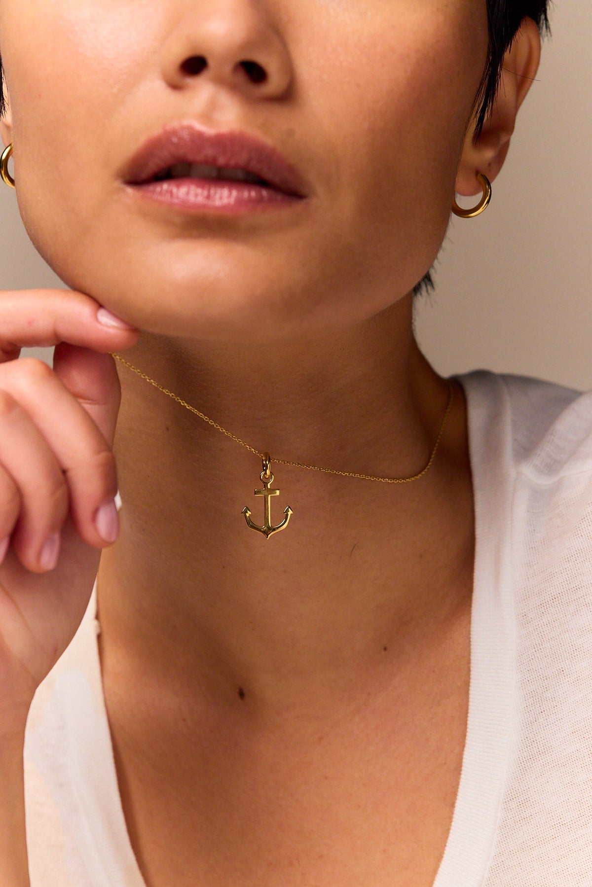 Small gold anchor pendant on trace chain necklace, close to neckline