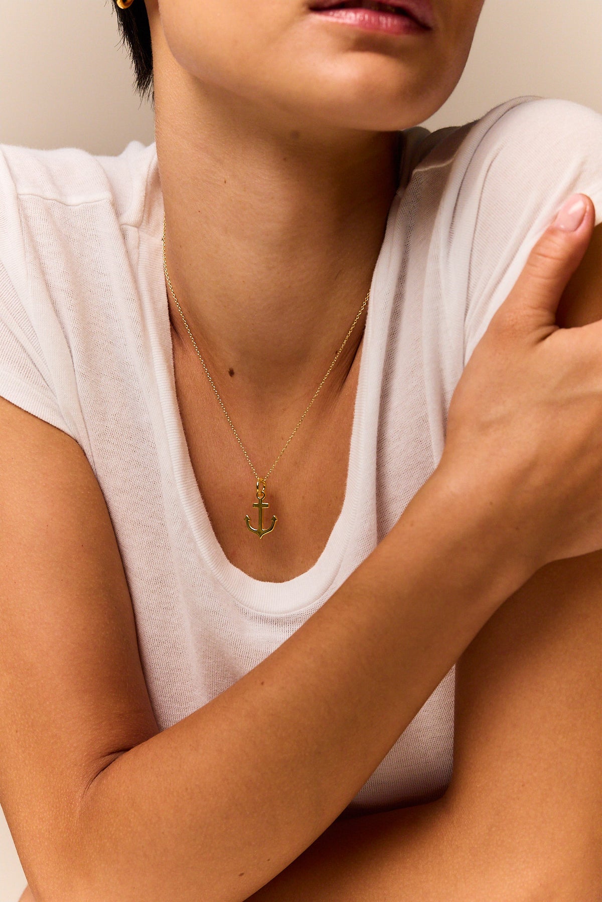 Gold anchor pendant necklace on trace chain, resting at upper chest