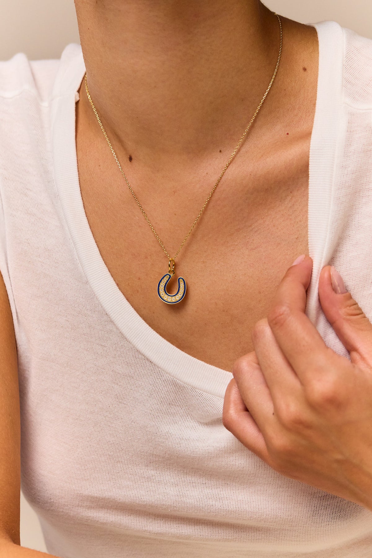 Gold horseshoe pendant necklace on trace chain, blue jeweled enamel detail