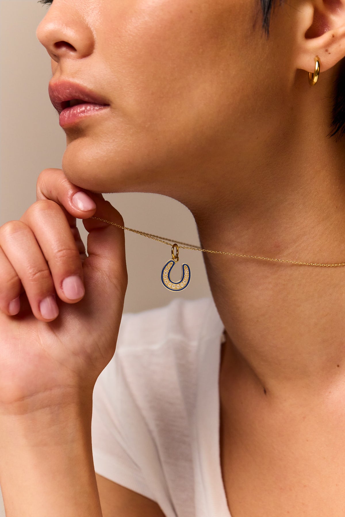 Gold horseshoe pendant necklace on trace chain, blue jeweled horseshoe at collar