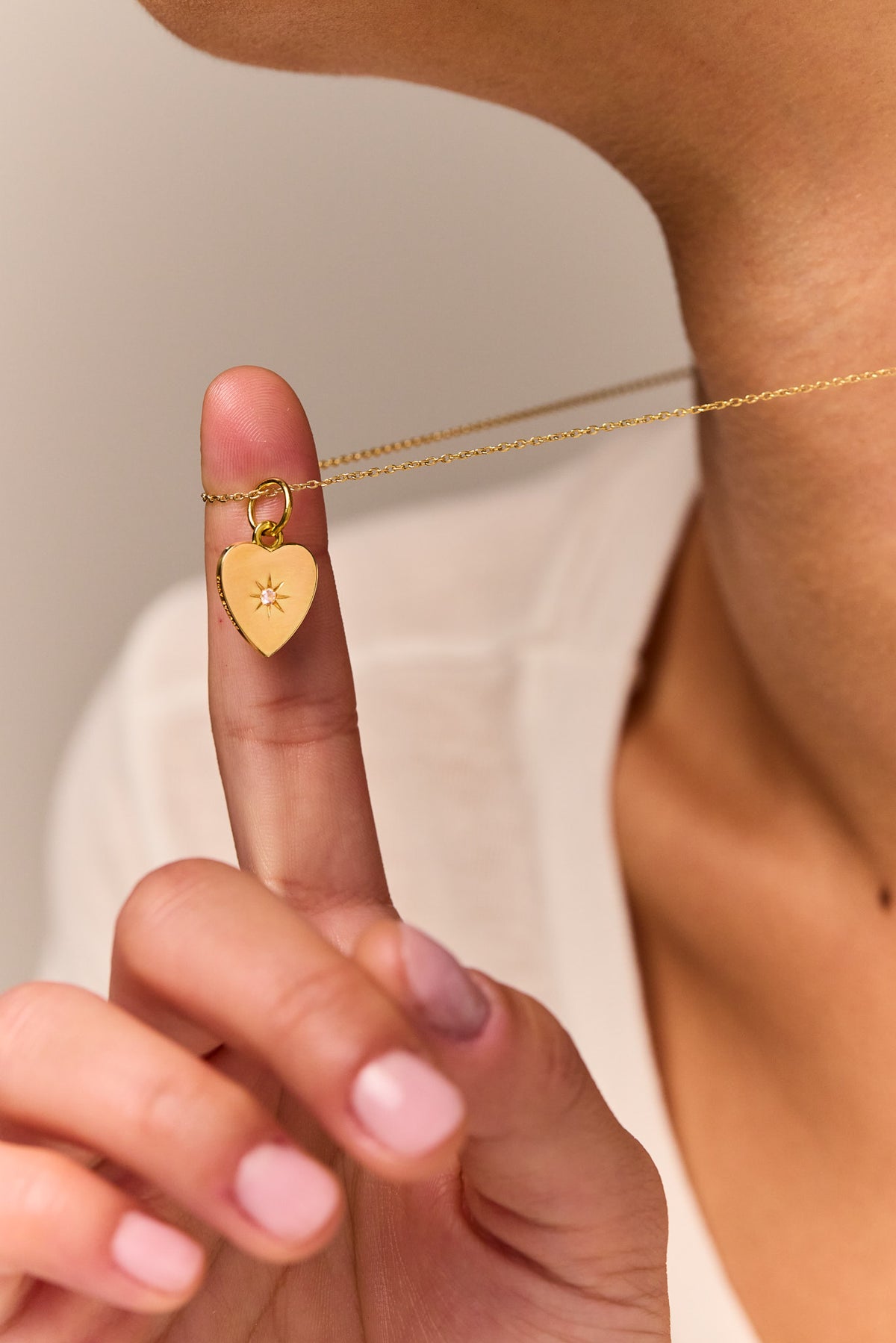 Gold heart pendant on fine trace chain, shown in hand