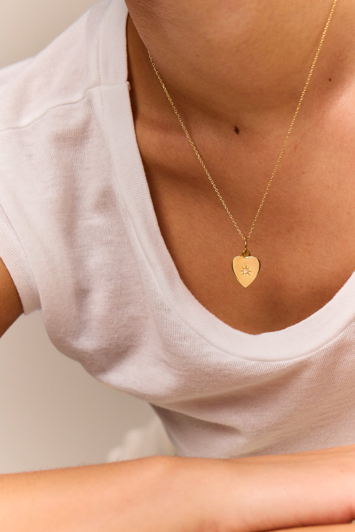 Gold heart pendant on trace chain necklace worn with white scoop-neck top