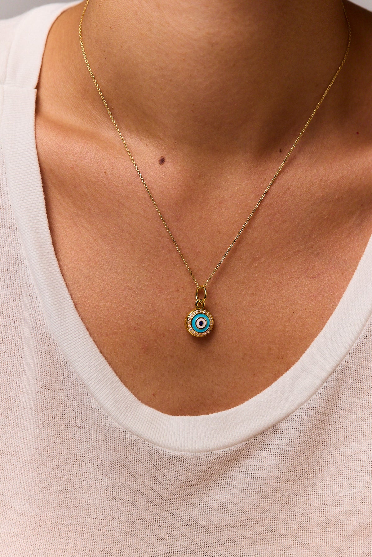 Gold evil eye pendant necklace with small blue enamel disc and gold ring