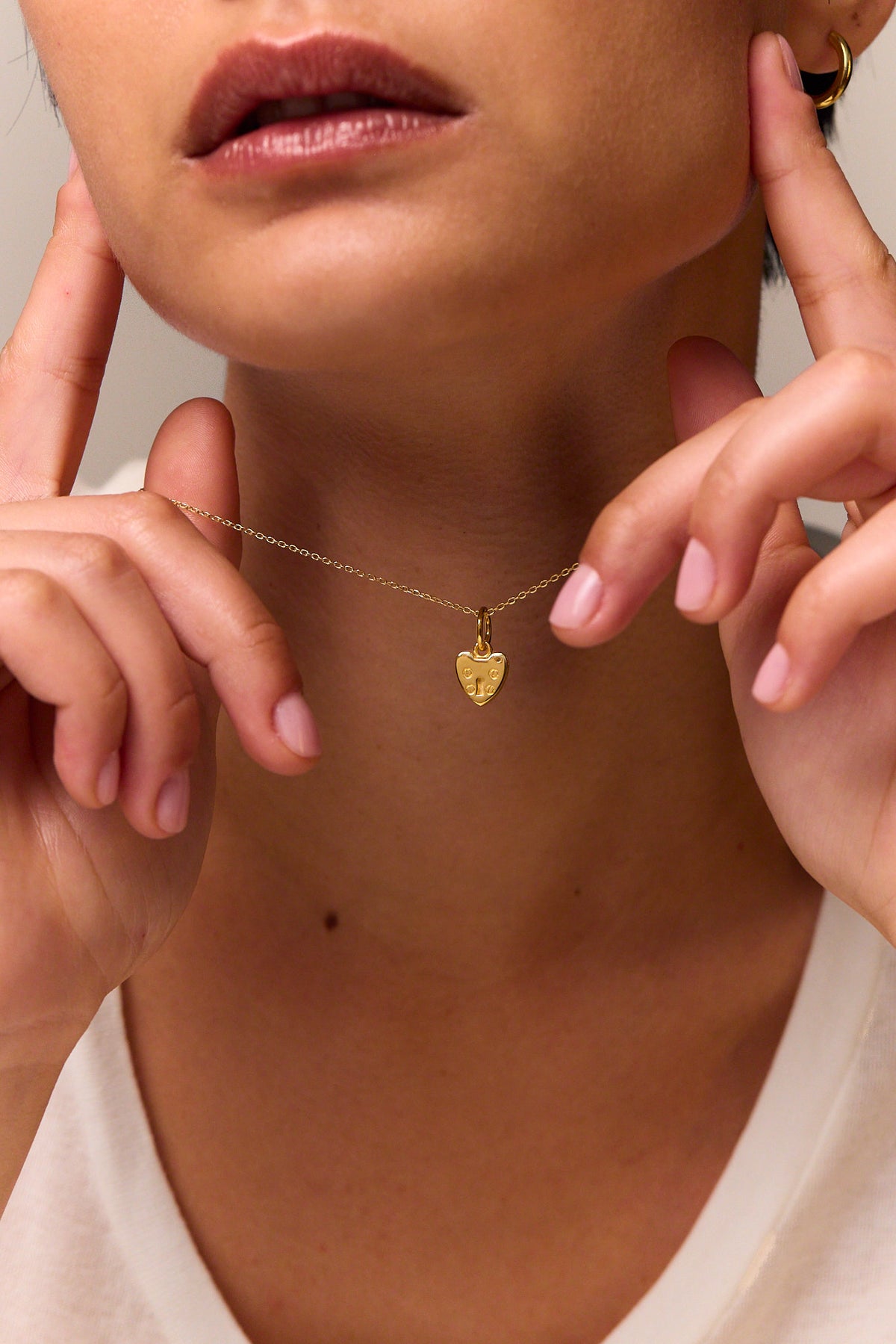 Gold heart padlock charm necklace on trace chain, worn at the collar