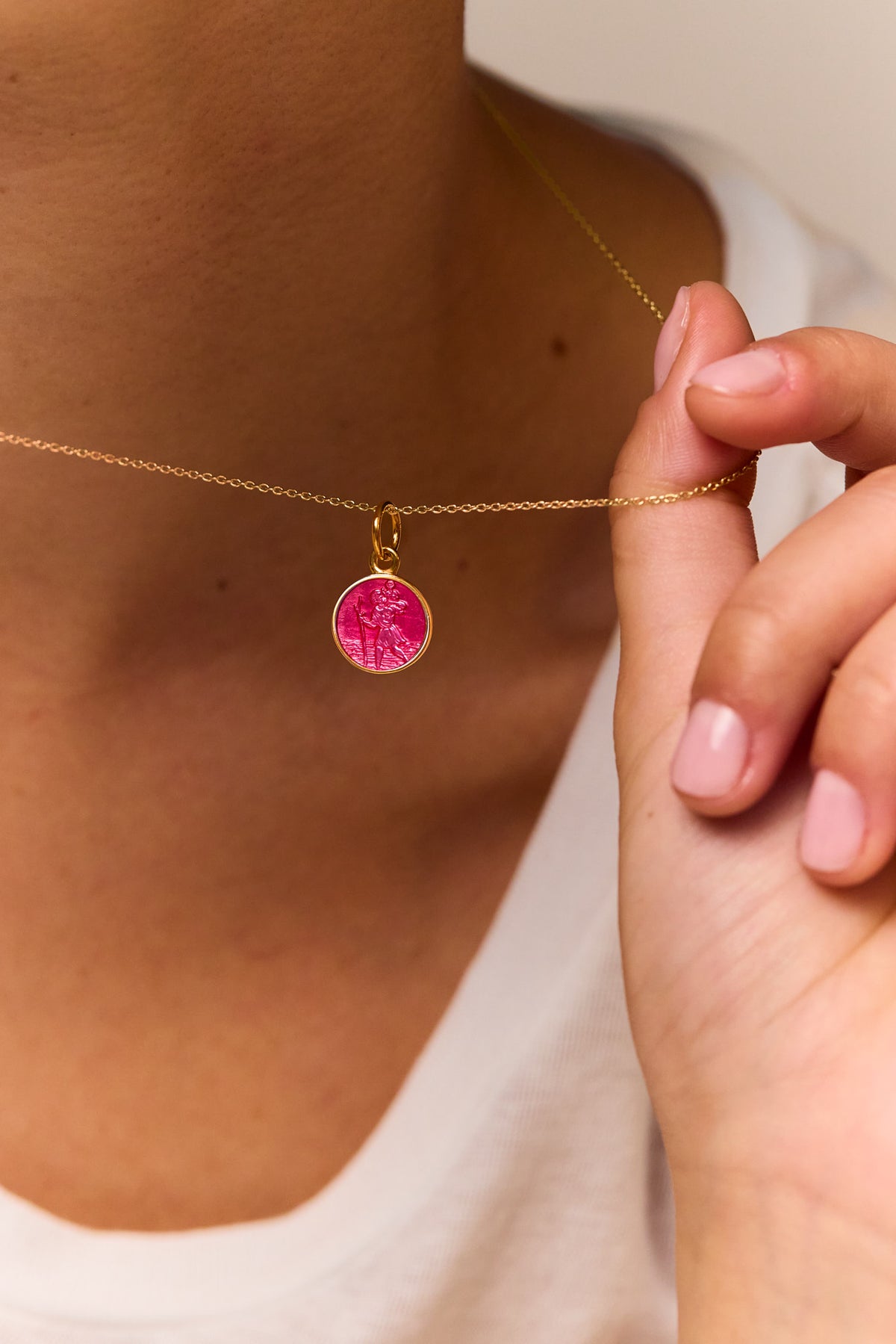 Gold chain necklace with pink St Christopher pendant held near collar