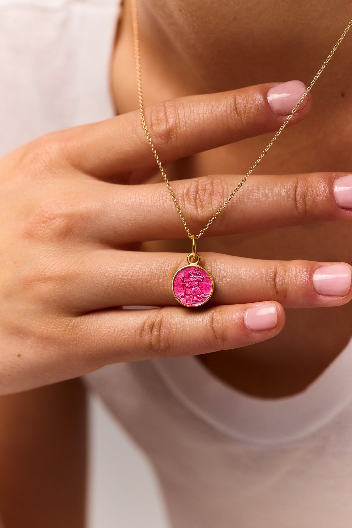 Gold trace chain necklace with pink St Christopher pendant centered in hands