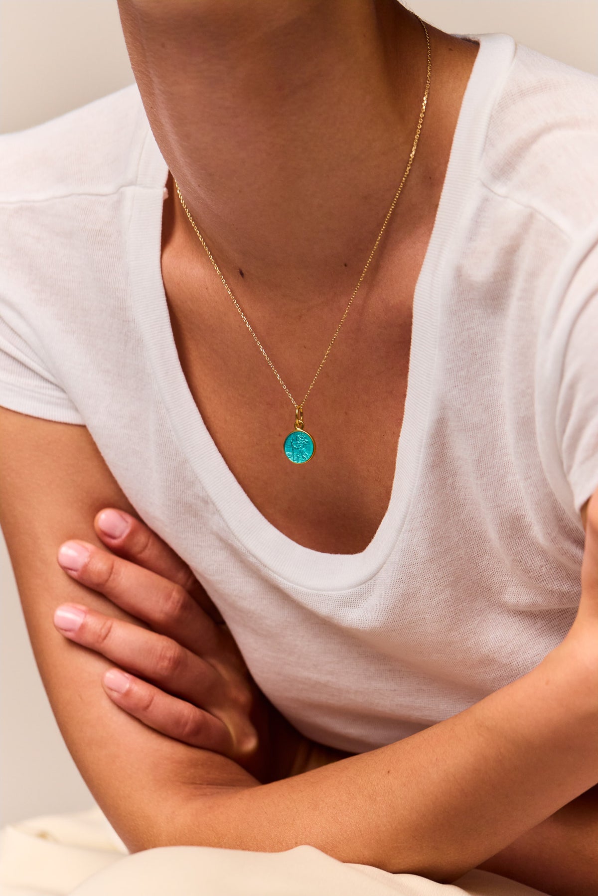 Gold trace chain necklace with turquoise St. Christopher medallion on chest