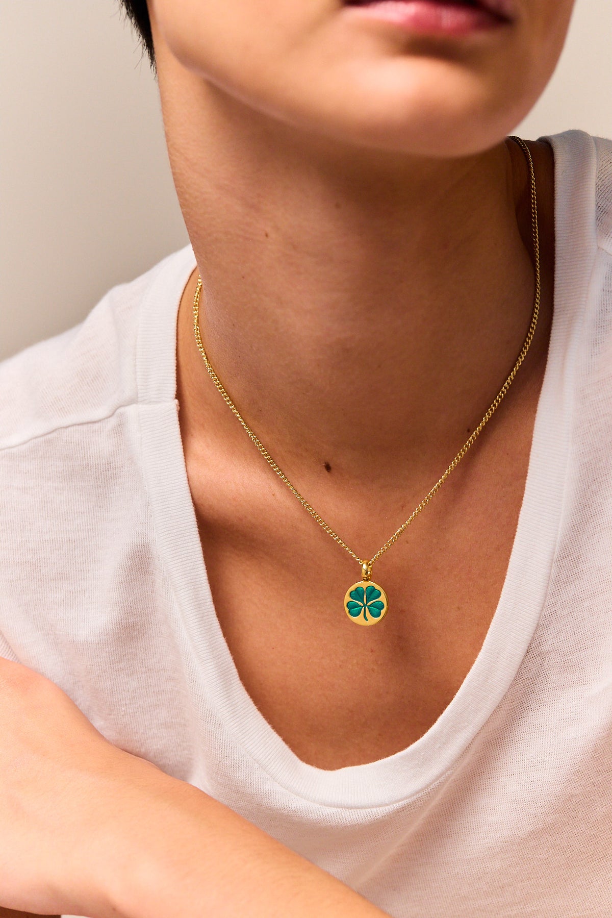 Gold clover pendant necklace with green enamel on fine curb chain, worn