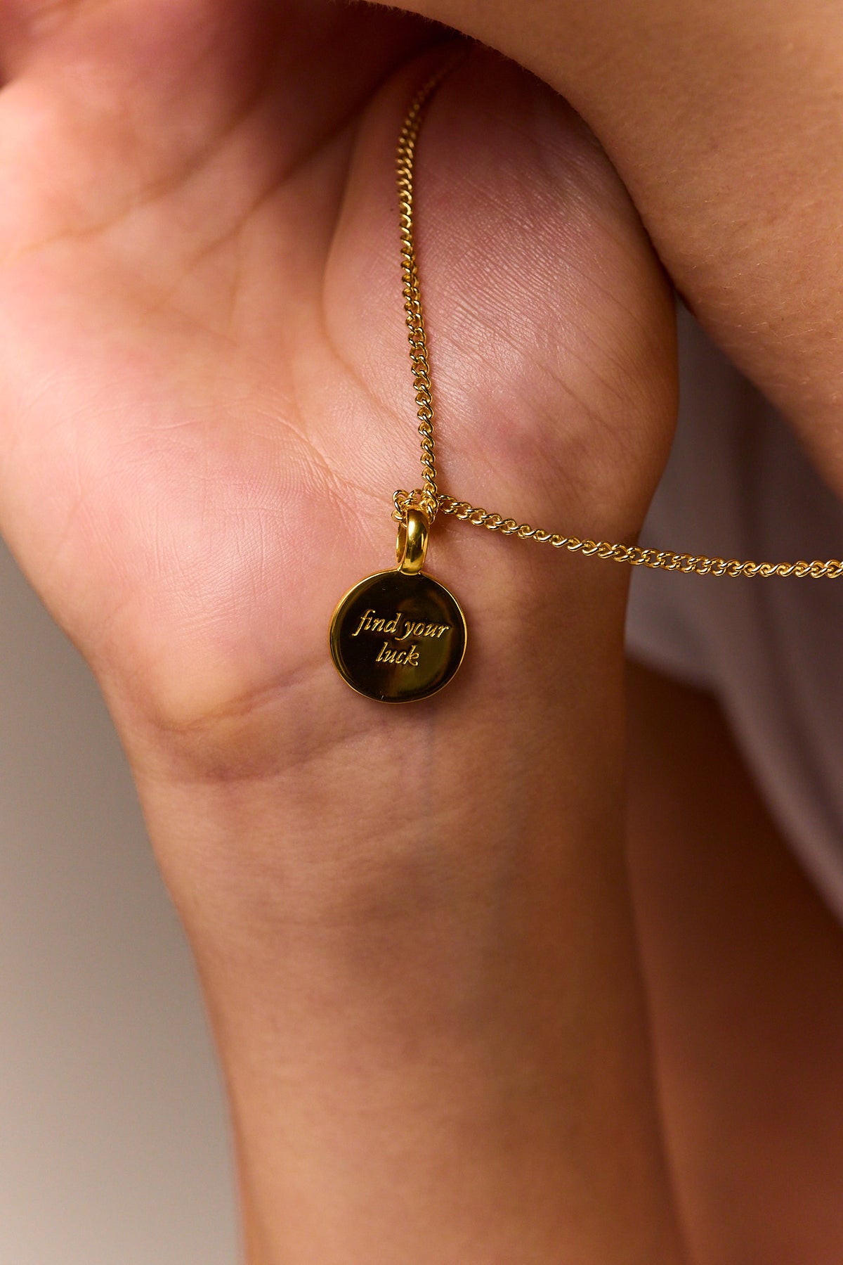 Gold curb-chain necklace with black round tag: “find your luck”