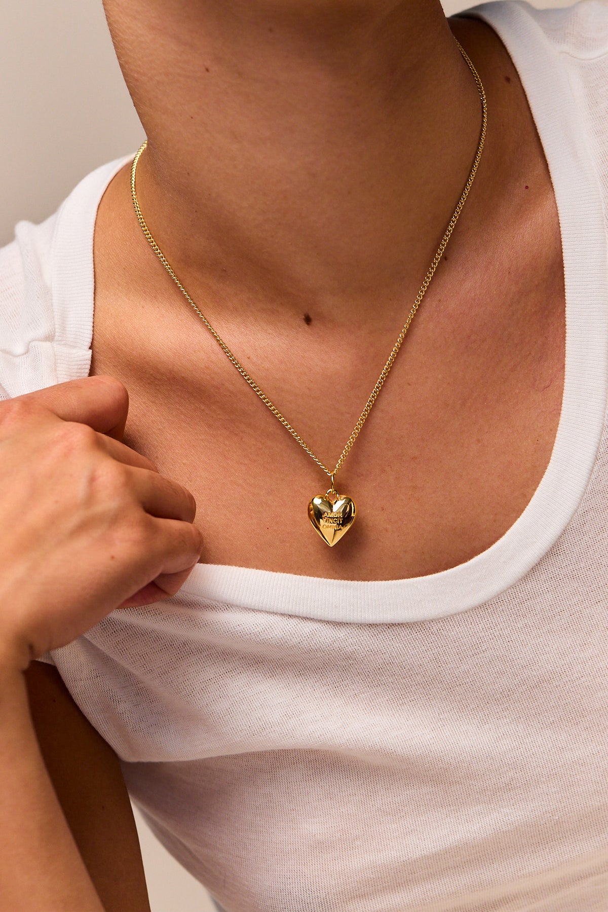 Gold heart pendant necklace on fine curb chain, worn at collarbone with engraved face