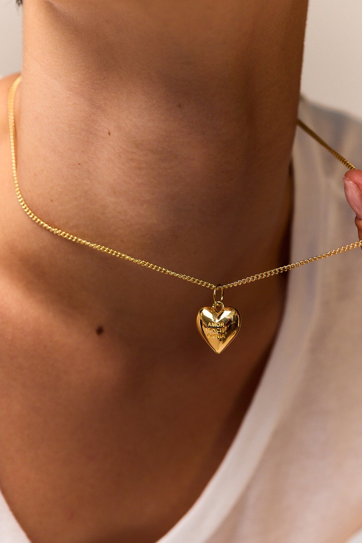 Gold heart pendant necklace on fine curb chain with small engraved text, close-up