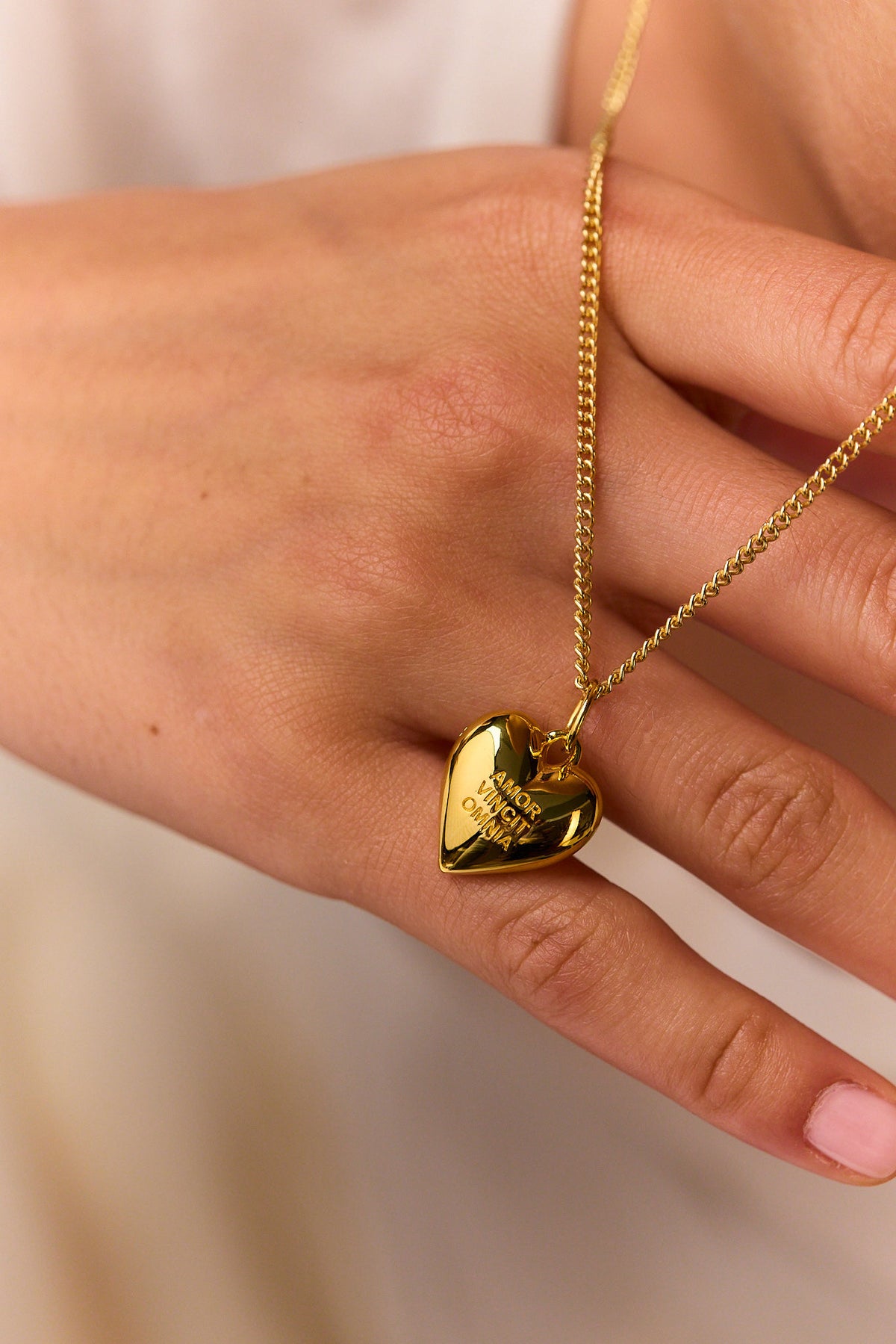 Gold heart pendant on fine curb chain held in hand, engraved lettering on face