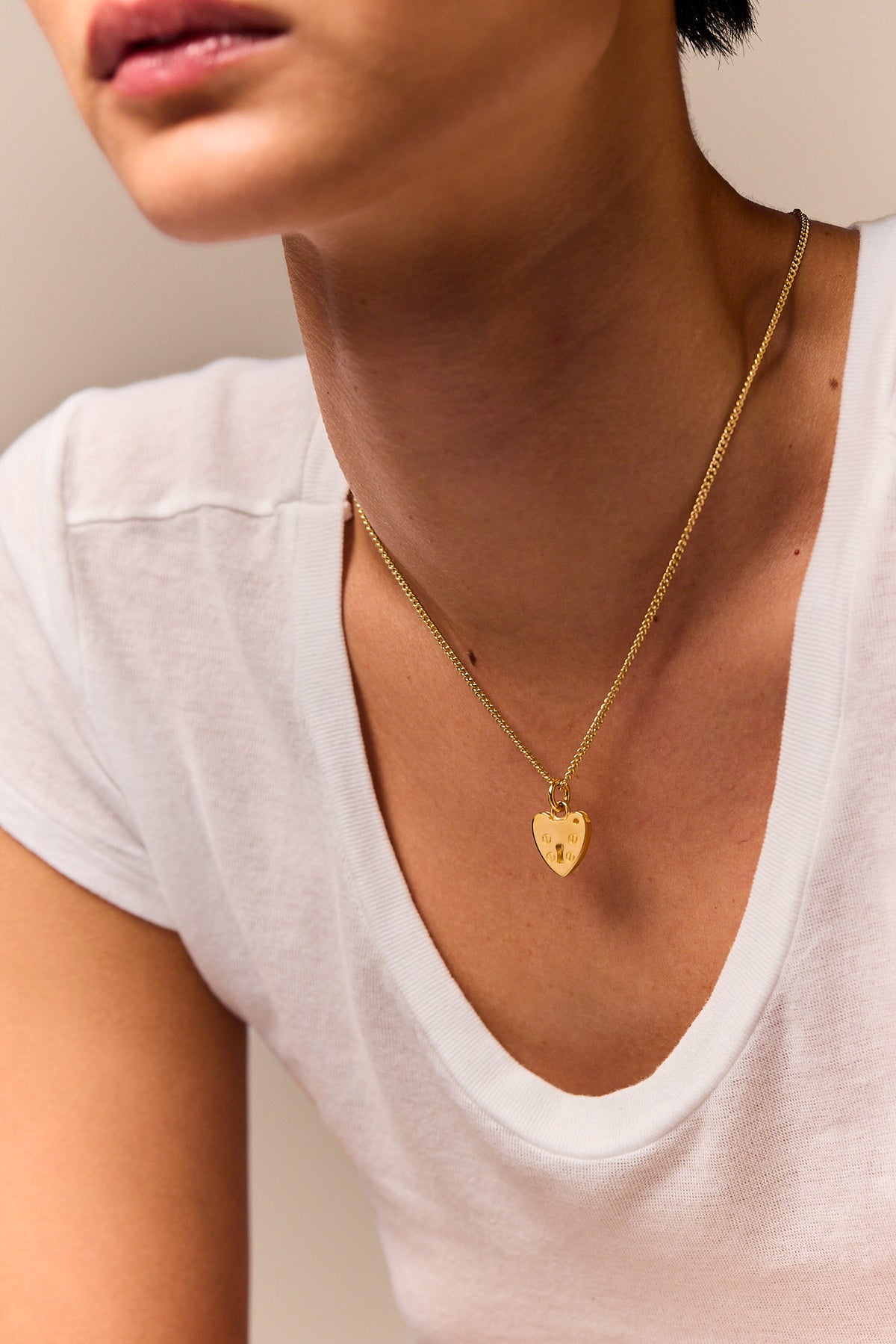 Gold heart padlock pendant necklace worn with fine curb chain