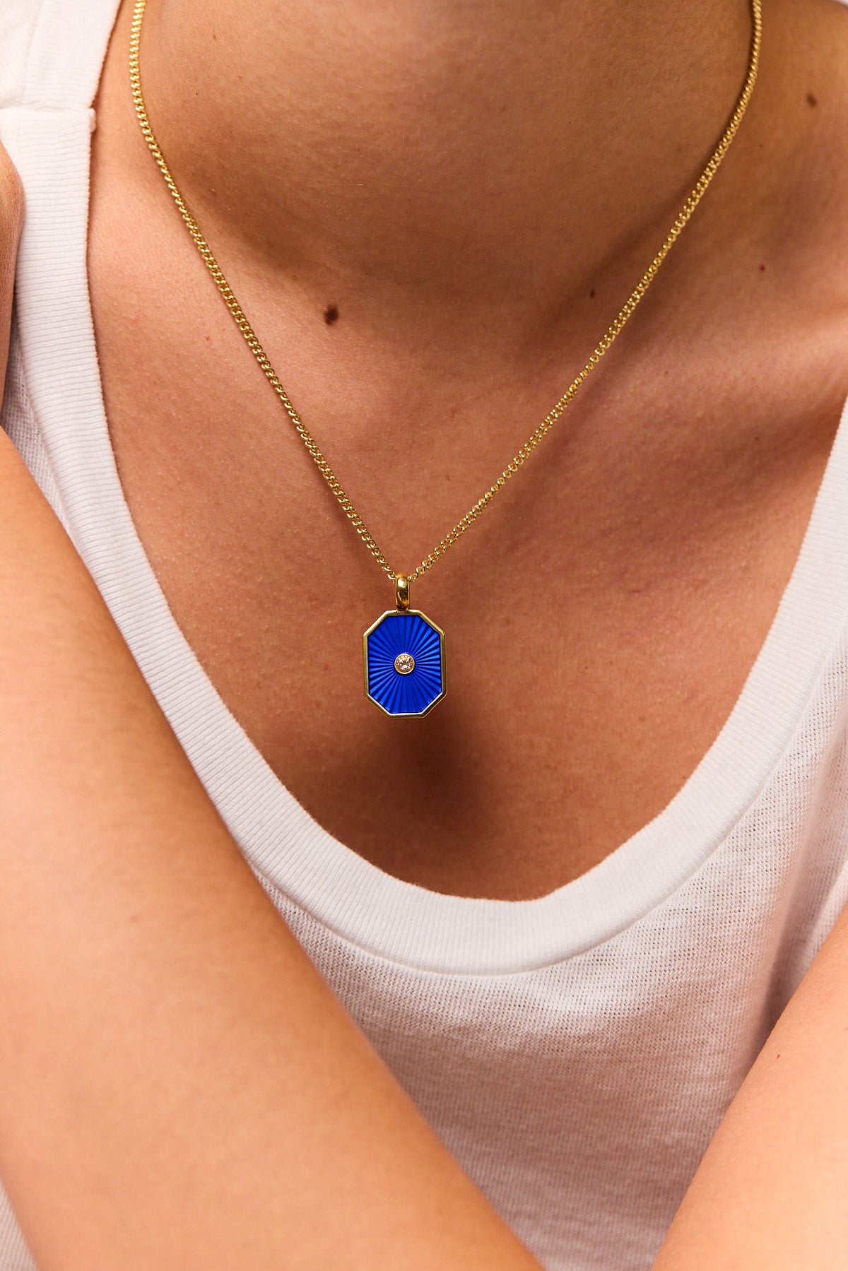 Gold necklace worn on neck with navy octagon pendant and round crystal