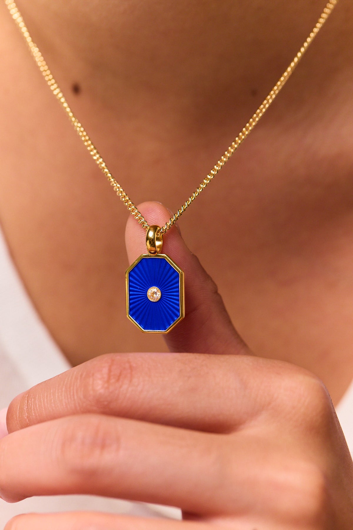 Close-up of gold chain necklace with navy octagon pendant and round center stone