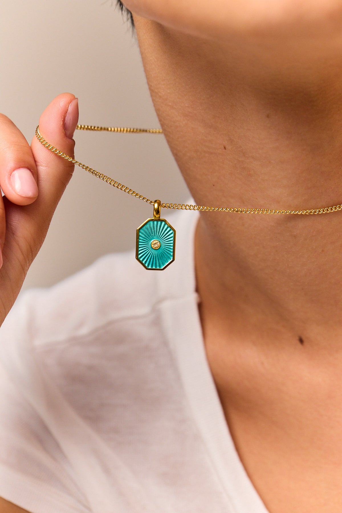 Turquoise octagon pendant on fine gold curb chain necklace, close-up held by hand