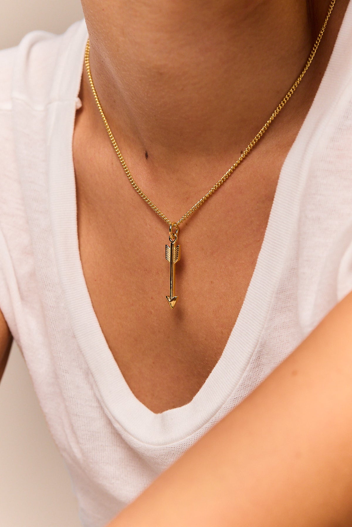 Gold arrow pendant necklace on fine curb chain, arrow charm centered on neckline