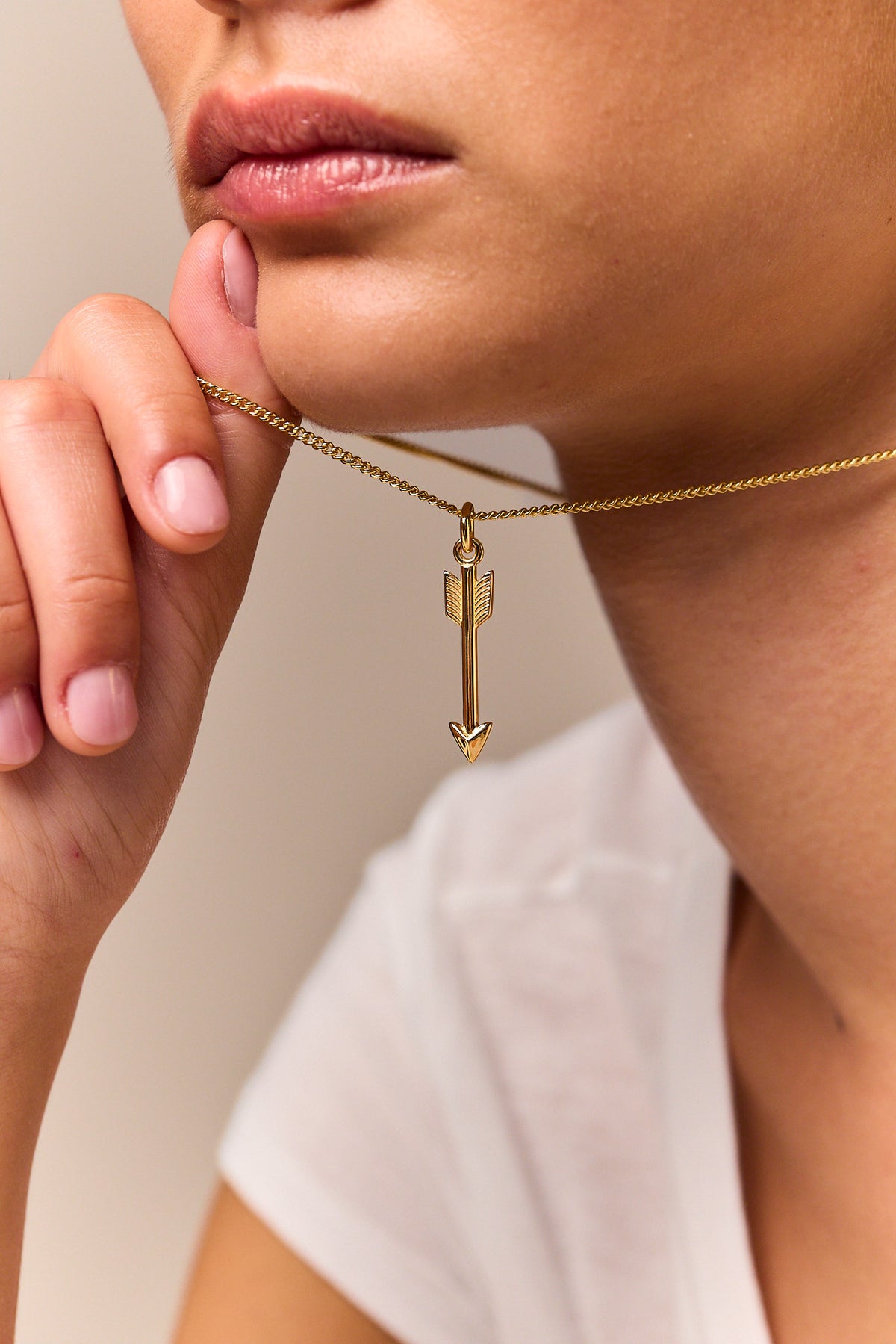 Gold arrow pendant necklace with fine curb chain, arrow charm held near collar