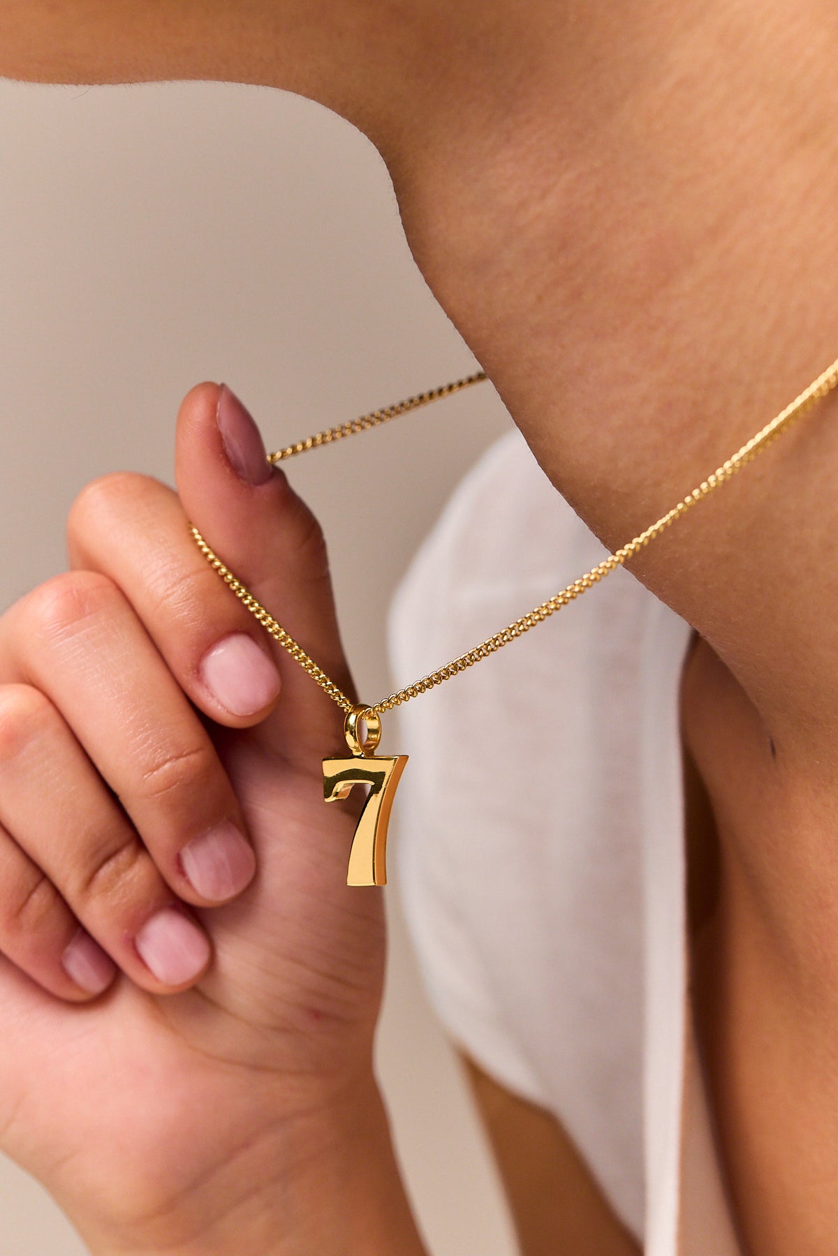Gold No 7 pendant necklace held in hand on fine curb chain.