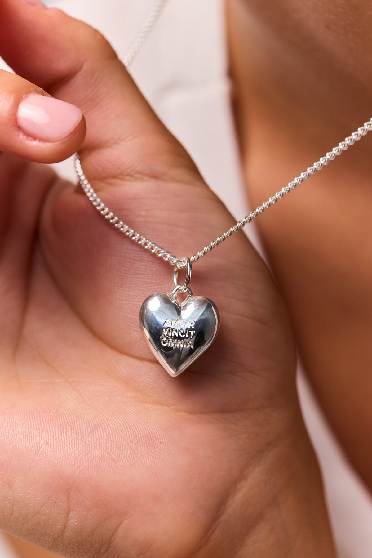Close-up of silver heart pendant on fine curb chain with blue engraved detail
