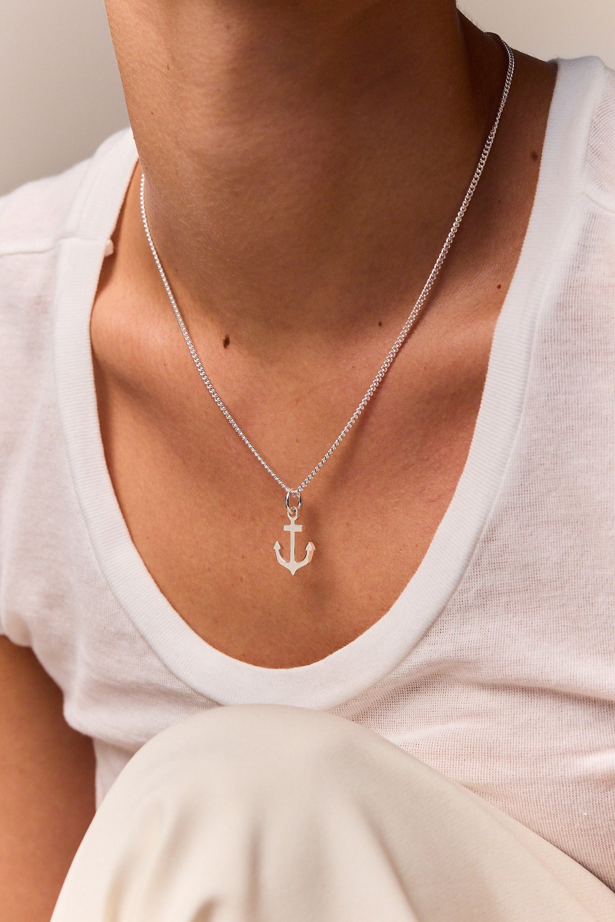 Silver anchor pendant on fine curb chain necklace worn with white shirt