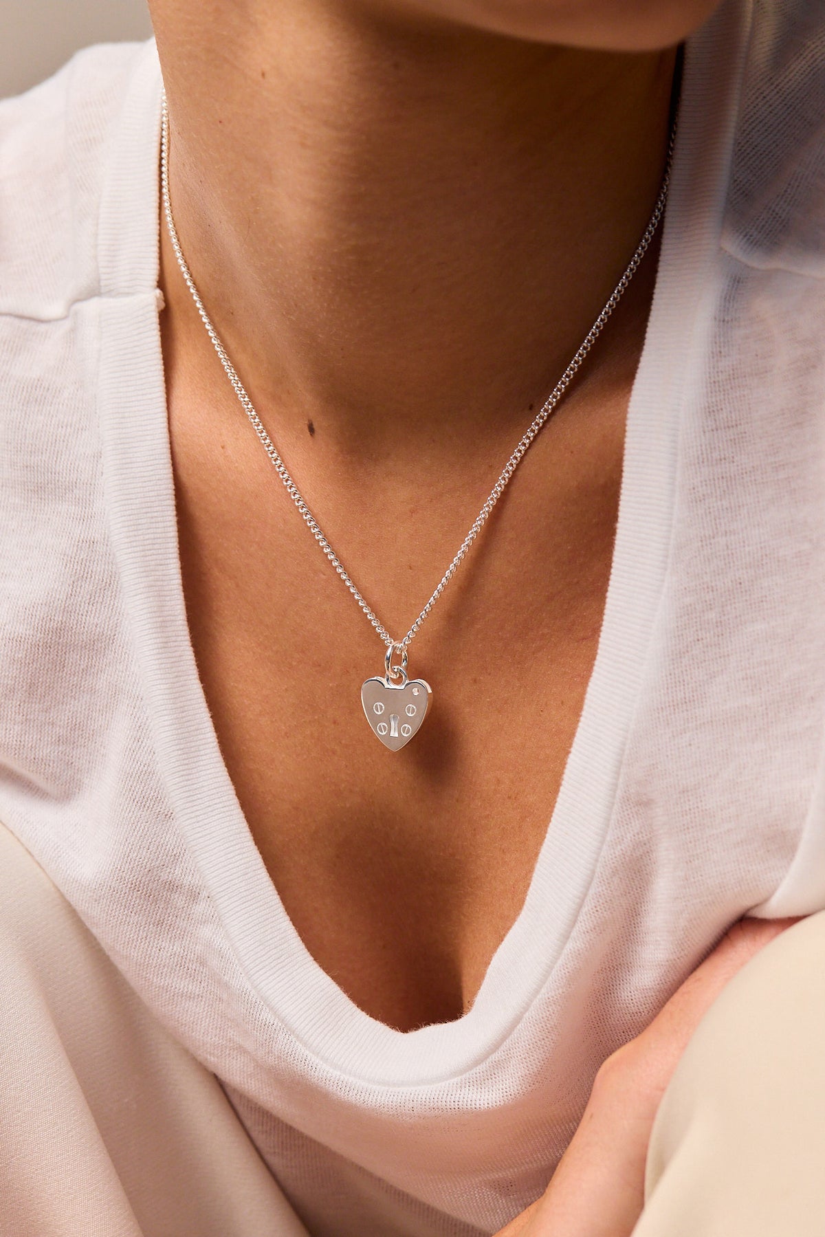 Silver heart padlock necklace with fine curb chain worn close to collar