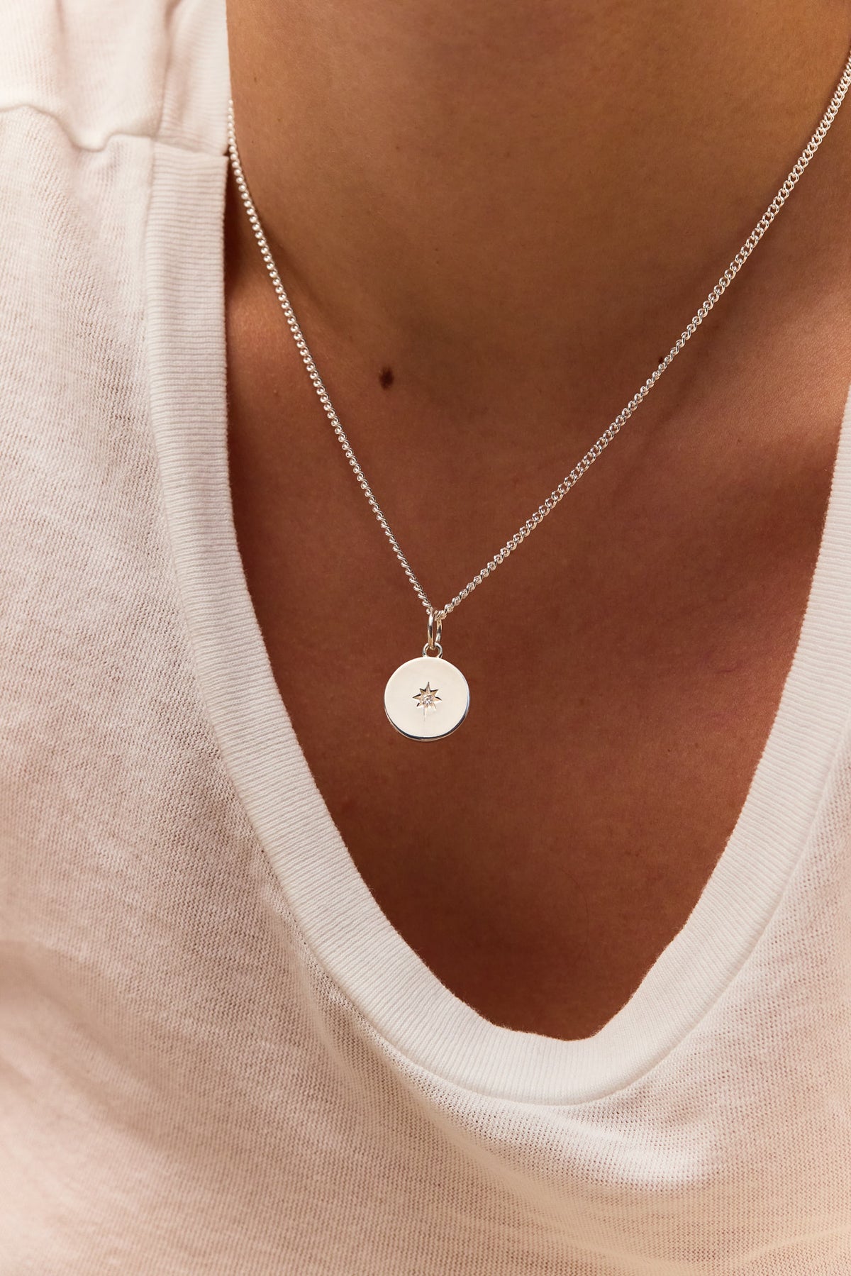 Silver star disc pendant necklace on fine curb chain, worn on neckline
