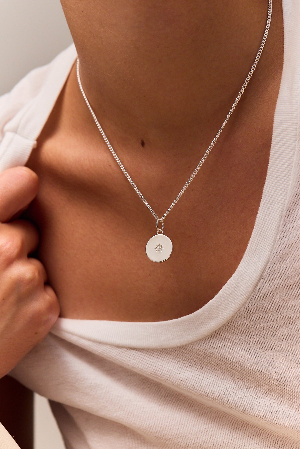 Silver disc pendant with star charm on fine curb chain, close view on chest