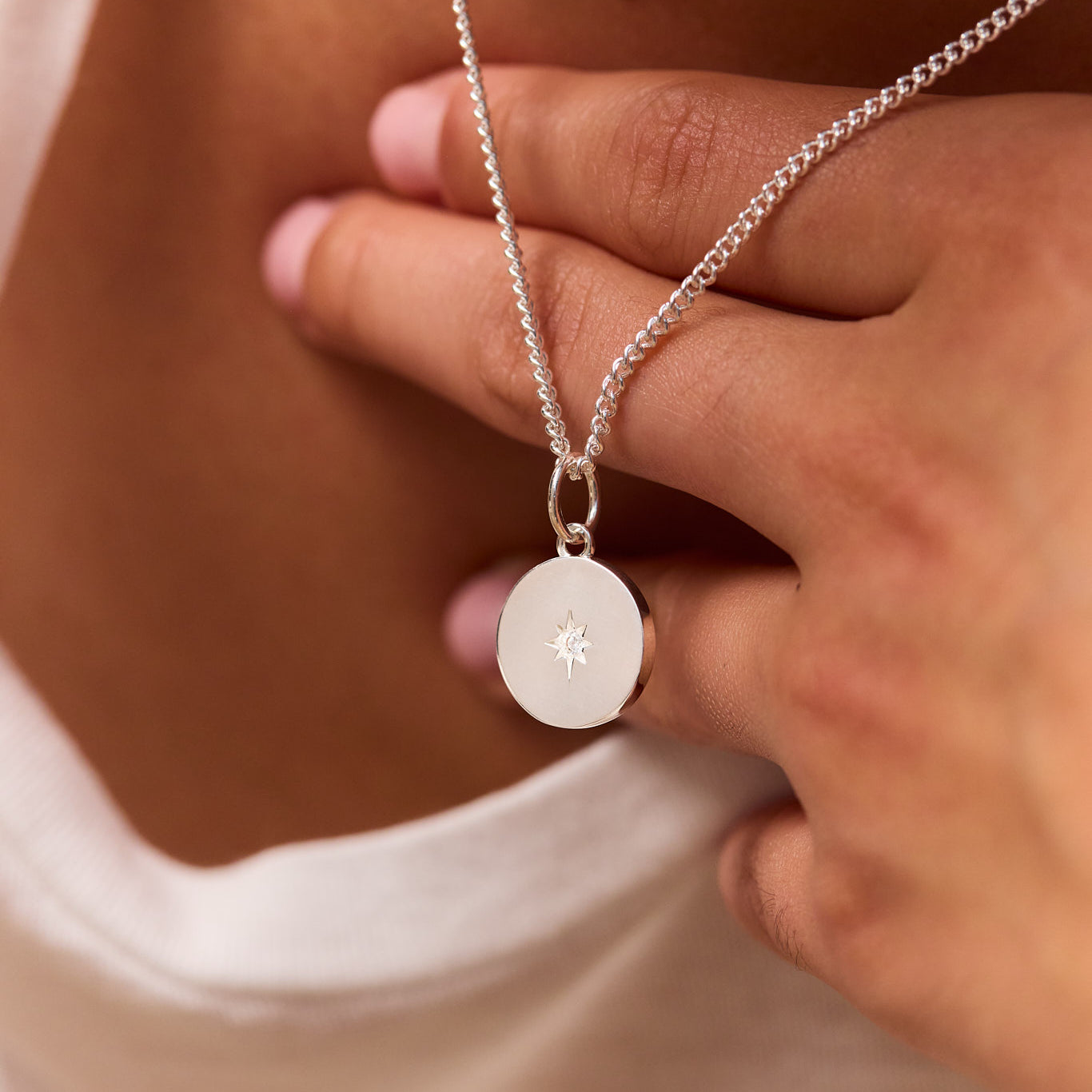 Silver fine curb chain with round disc pendant and star emblem, held near clasp