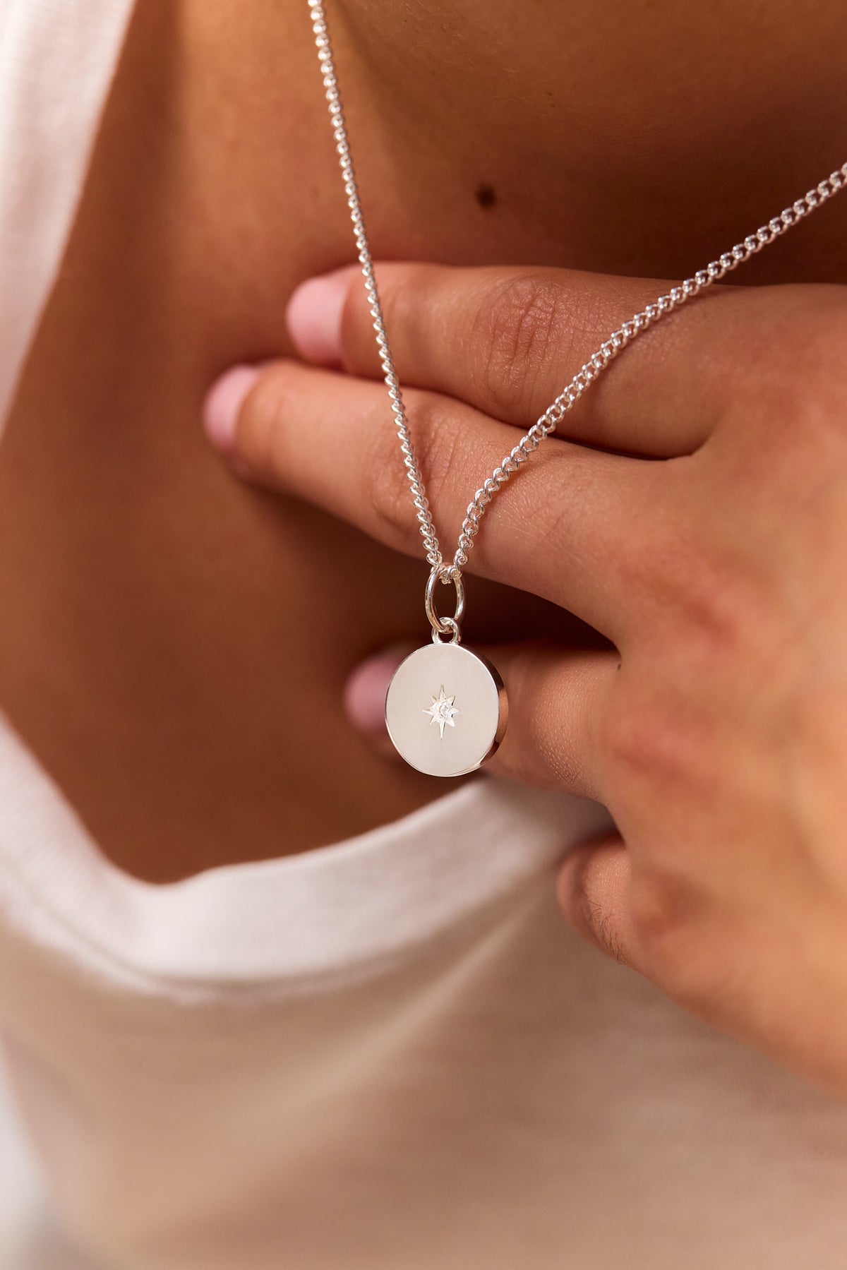 Silver fine curb chain with round disc pendant and star emblem, held near clasp