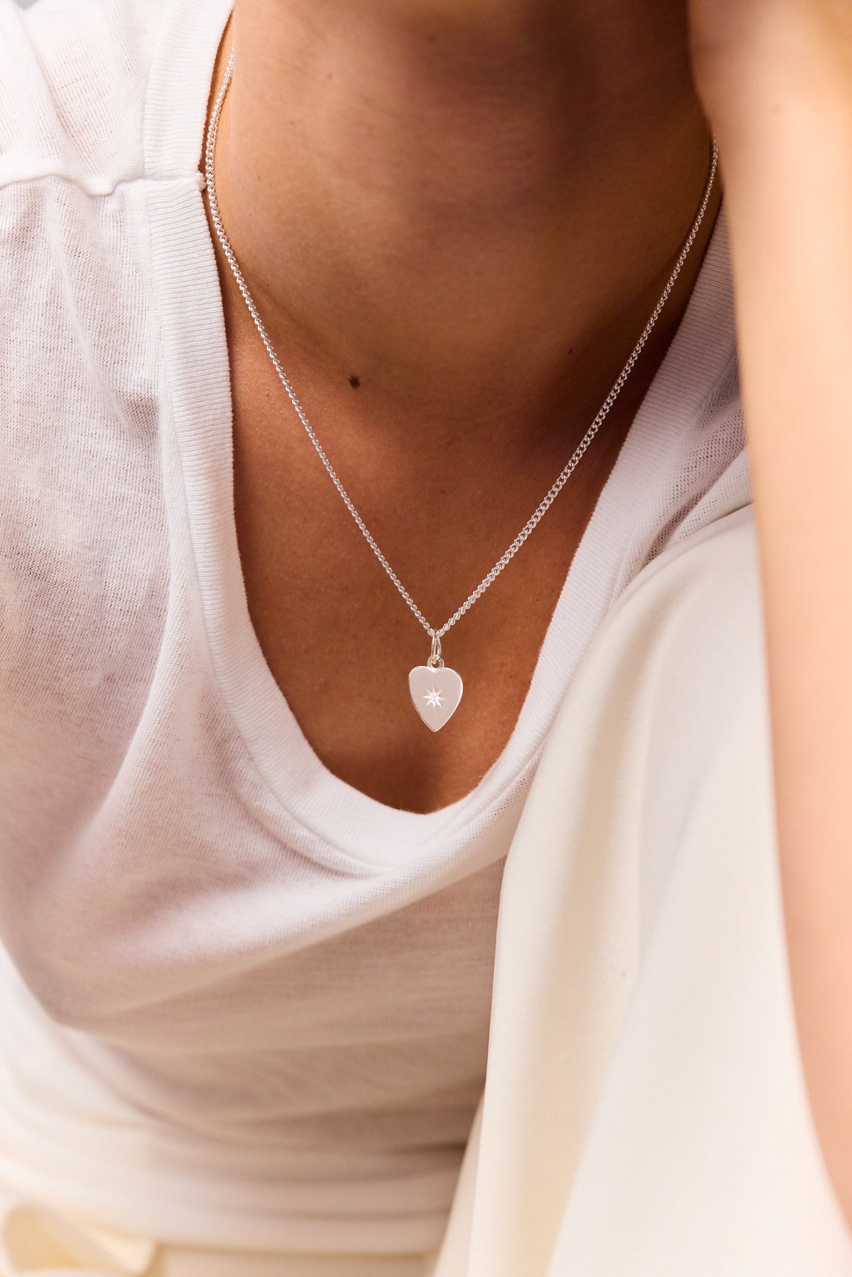 Silver heart pendant on fine curb chain necklace, shown on neckline.