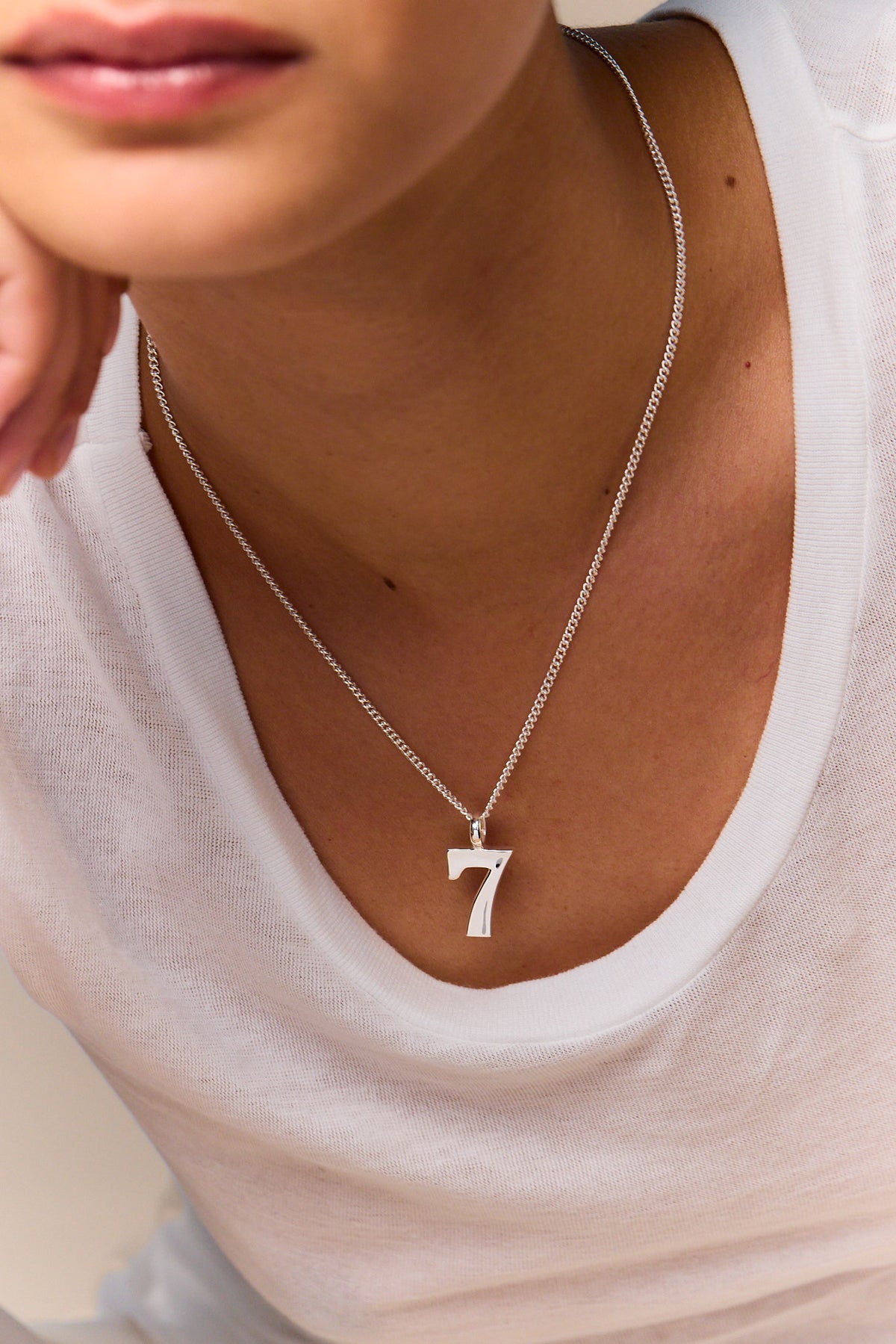 Silver number 7 pendant necklace on fine curb chain, worn on neckline