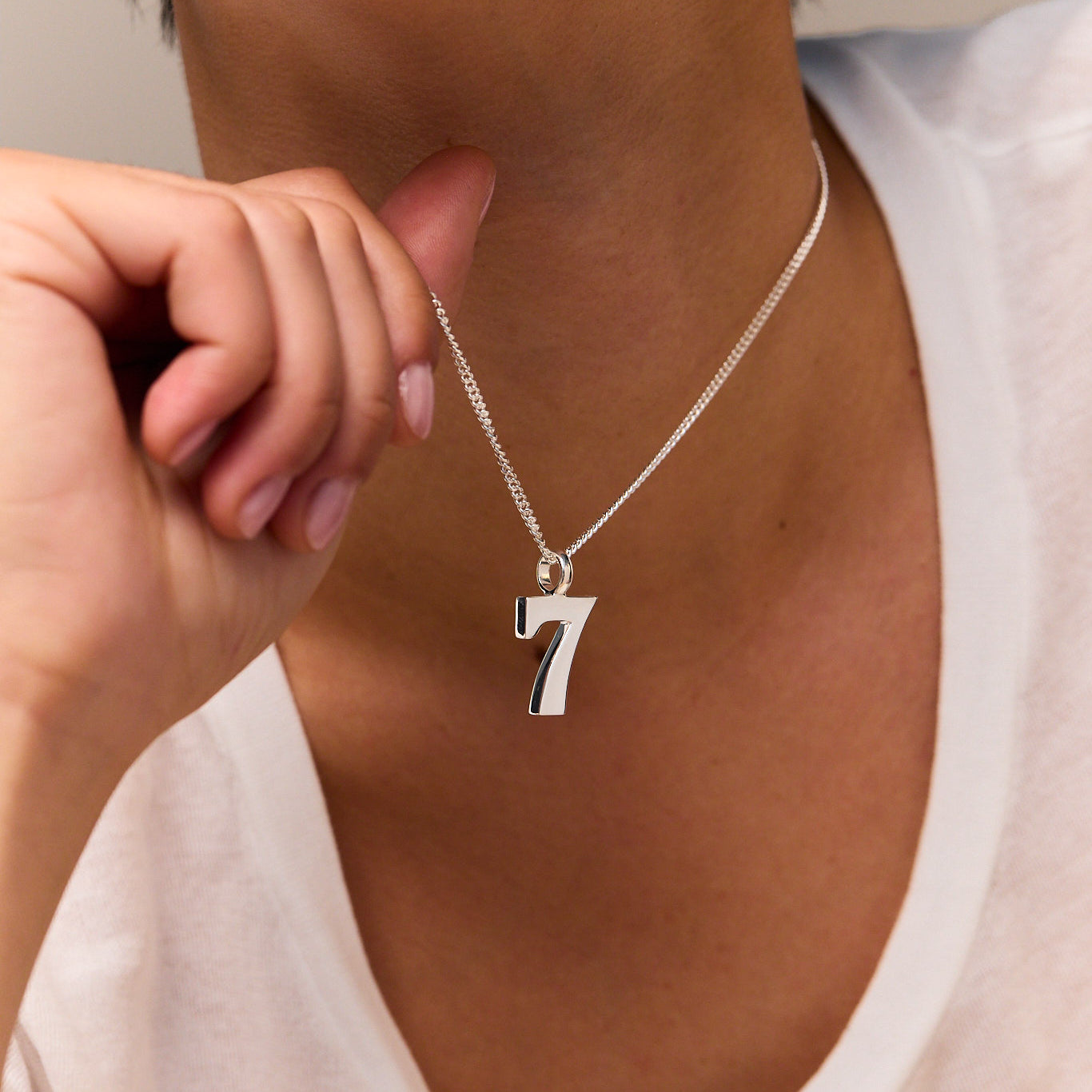 Silver number 7 pendant on fine curb chain necklace, held near neck