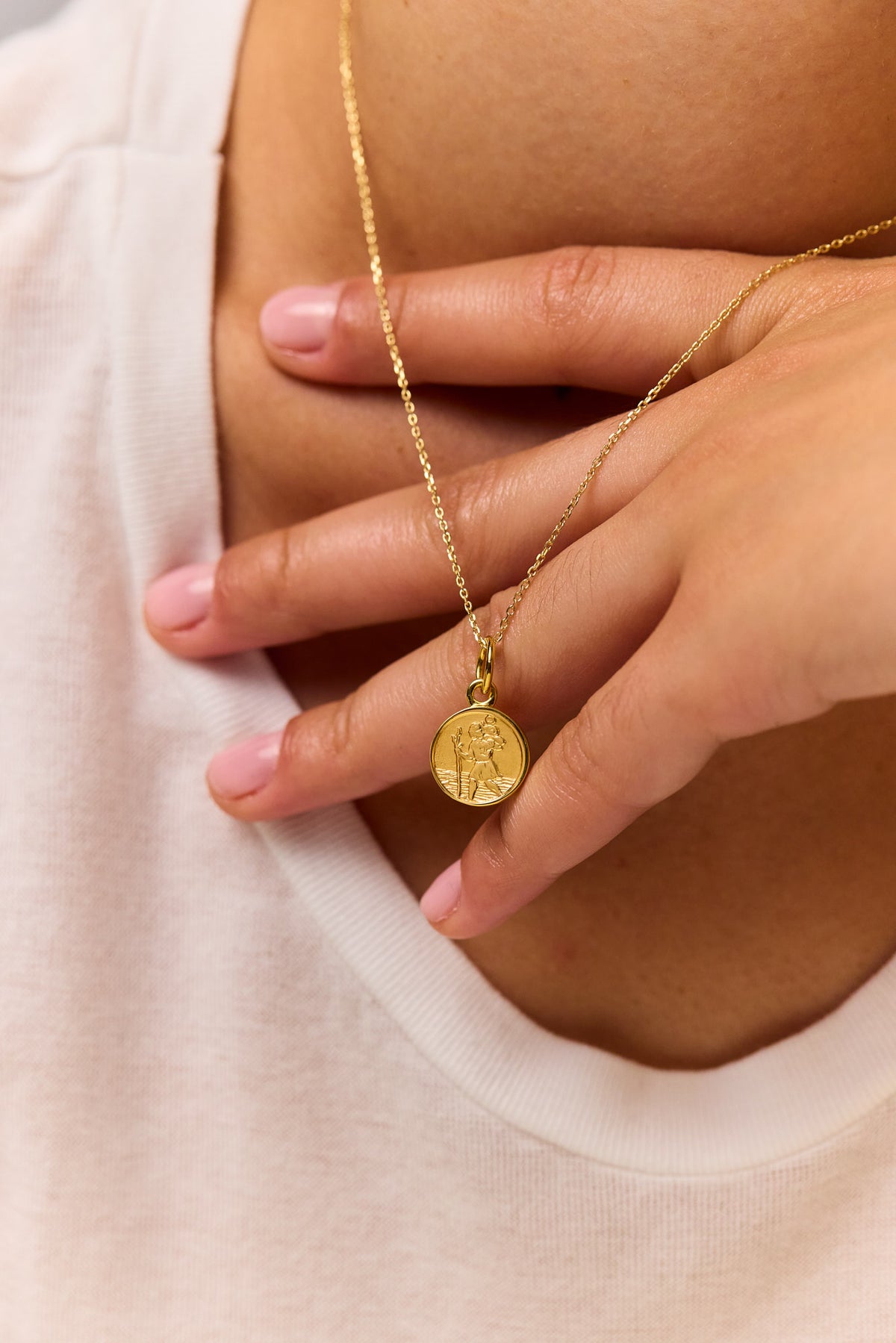 Gold trace chain necklace with round St Christopher charm pendant held in model hands