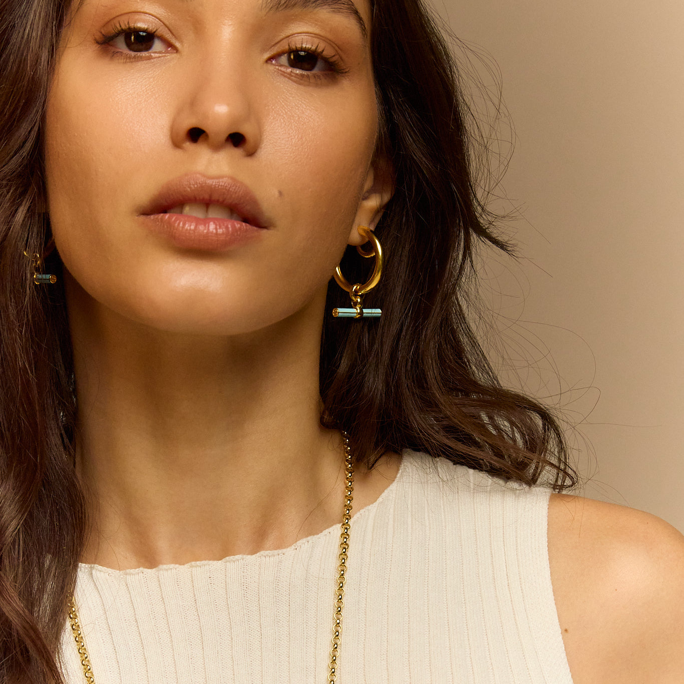 Gold hoop earrings with blue enamel T-bar charm worn near neck