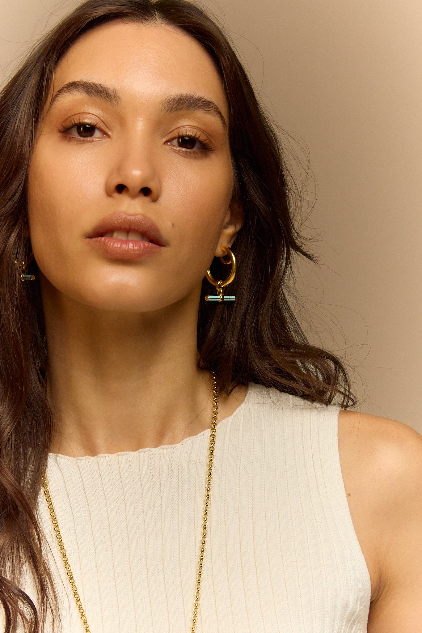 Gold hoop earrings with blue enamel T-bar charm worn near neck