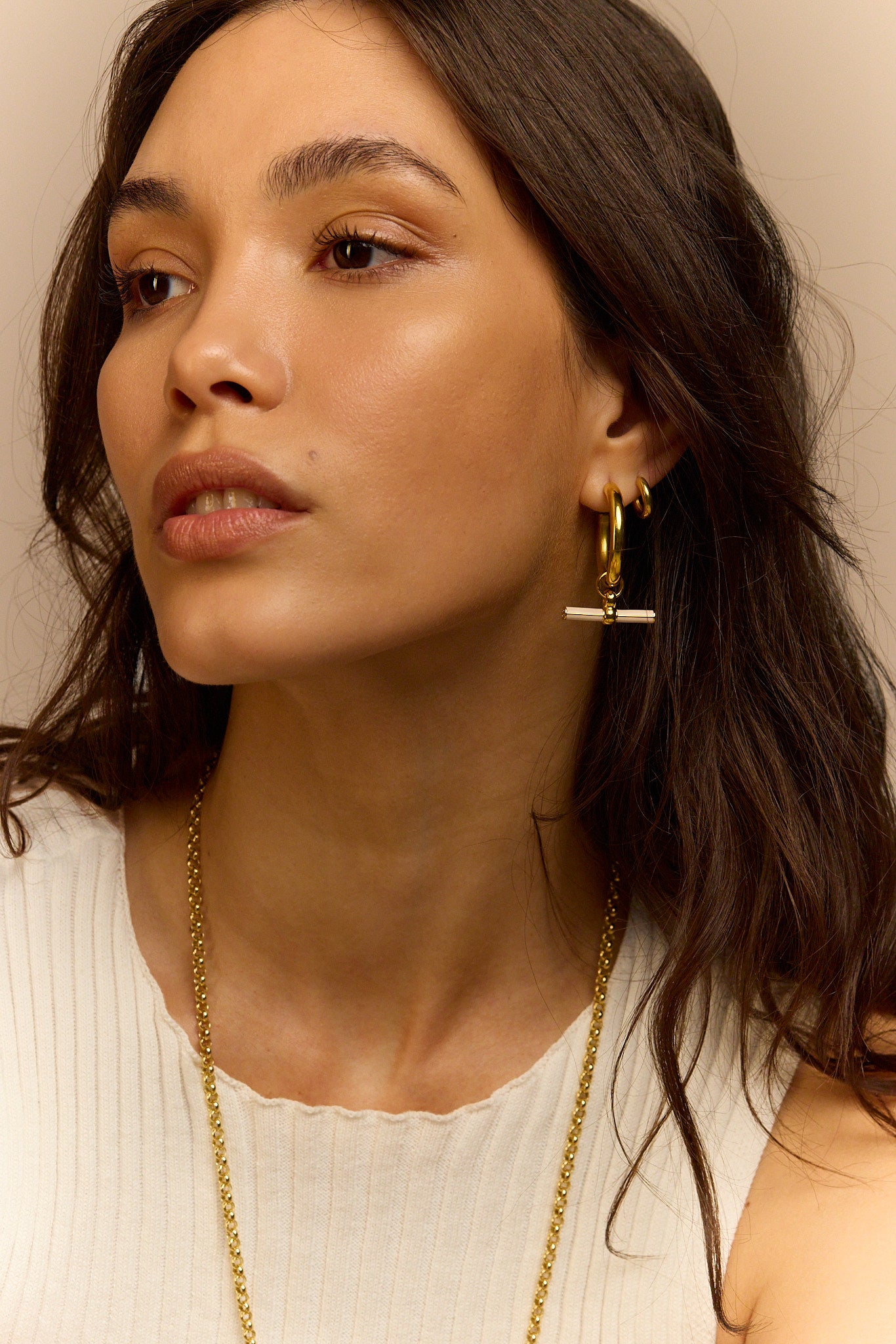 Gold-tone hoop earrings with cream enamel T-bar dangles, side view on model