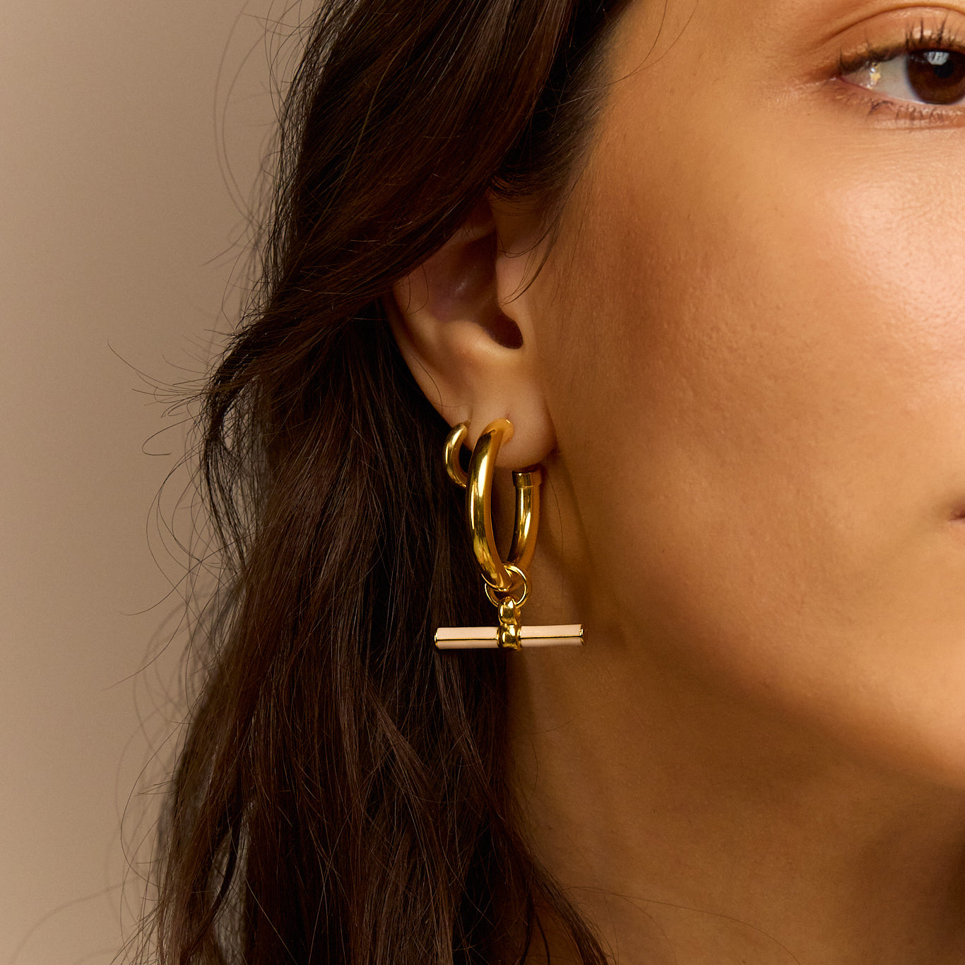 Gold-tone hoop earrings with cream enamel T-bar dangle, close side on model