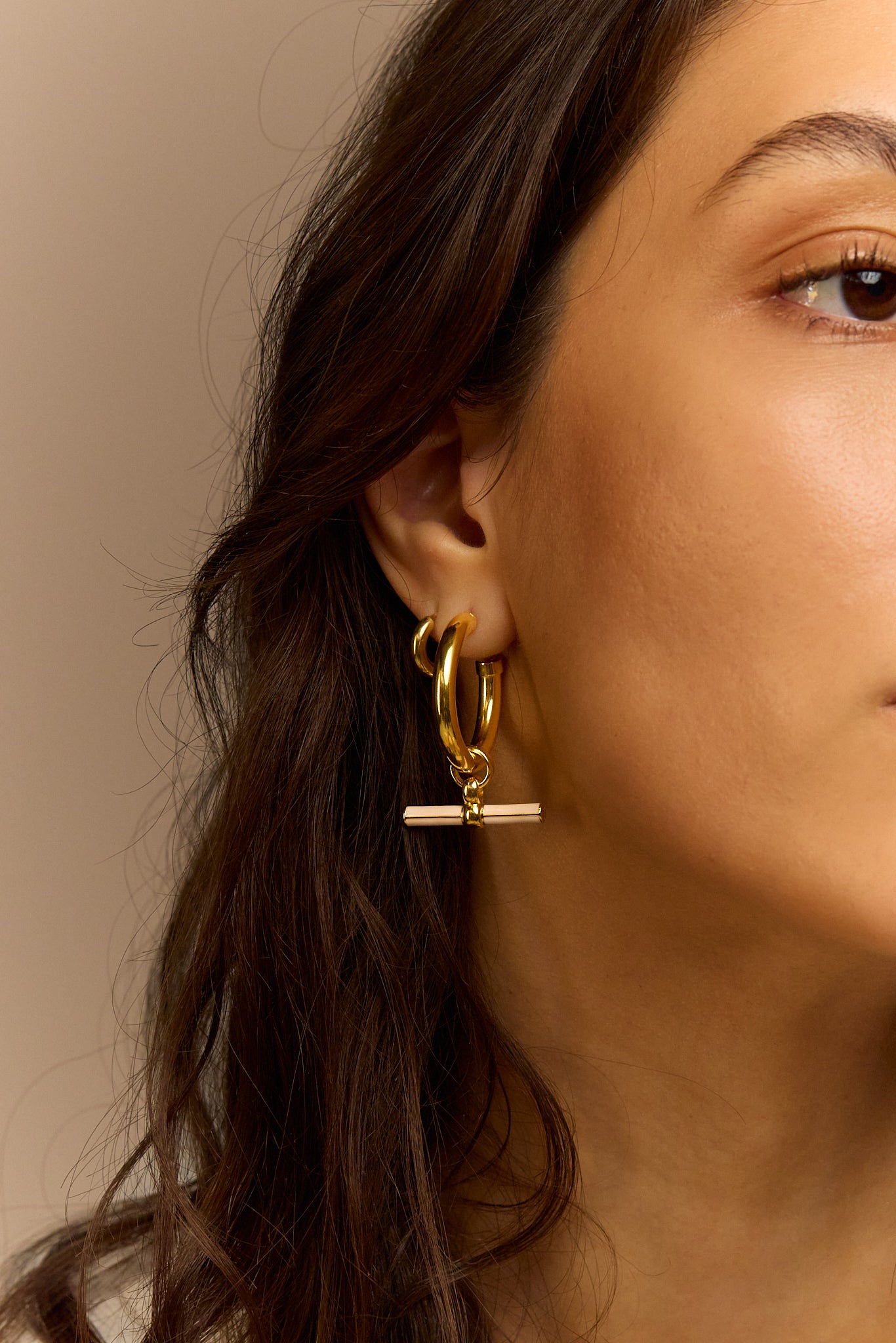 Gold-tone hoop earrings with cream enamel T-bar dangle, close side on model