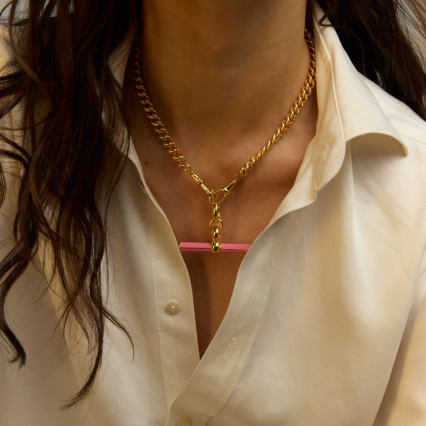 Gold chain necklace with pink enamel bar pendant, close-up at collar