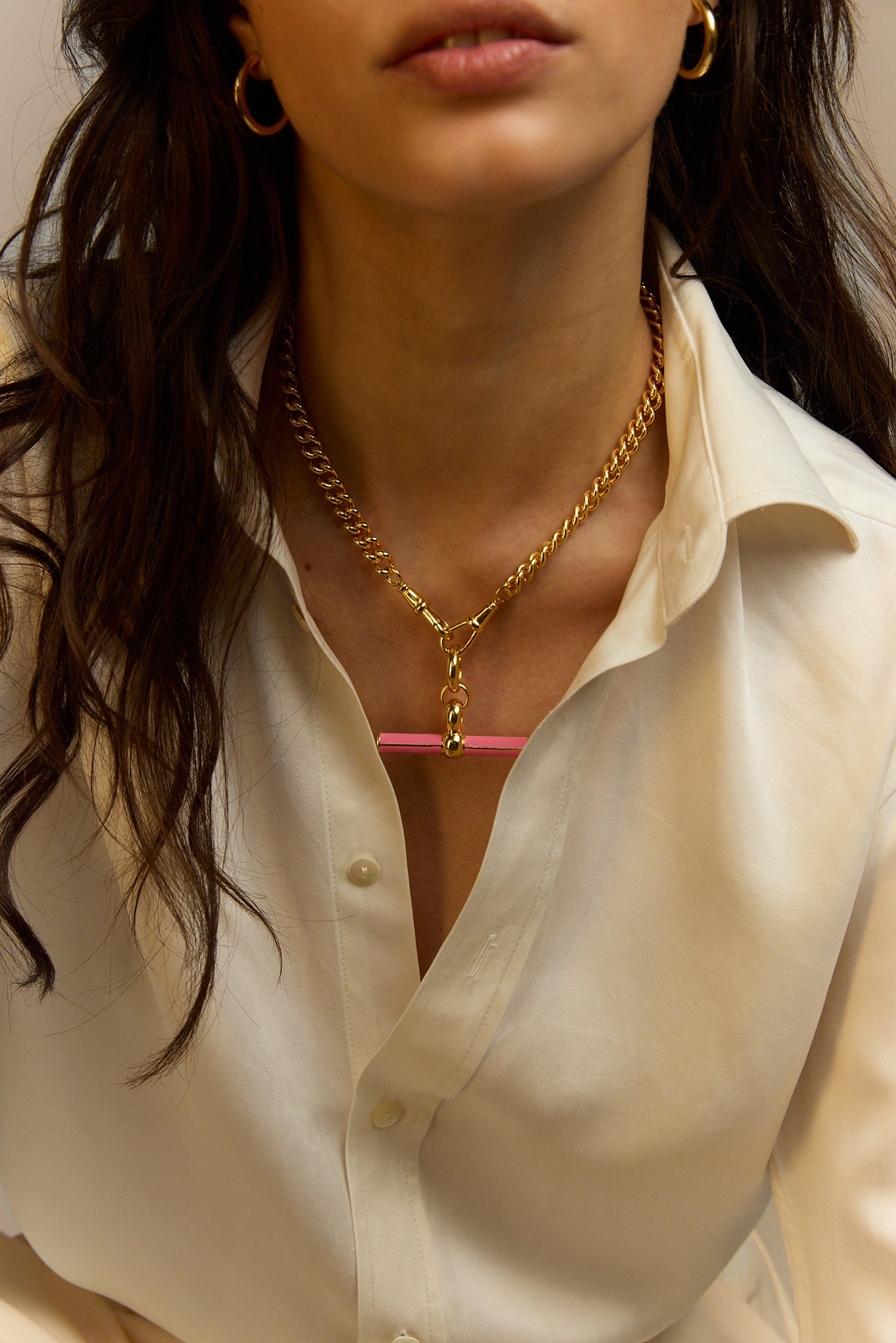 Gold chain necklace with pink enamel bar pendant, close-up at collar