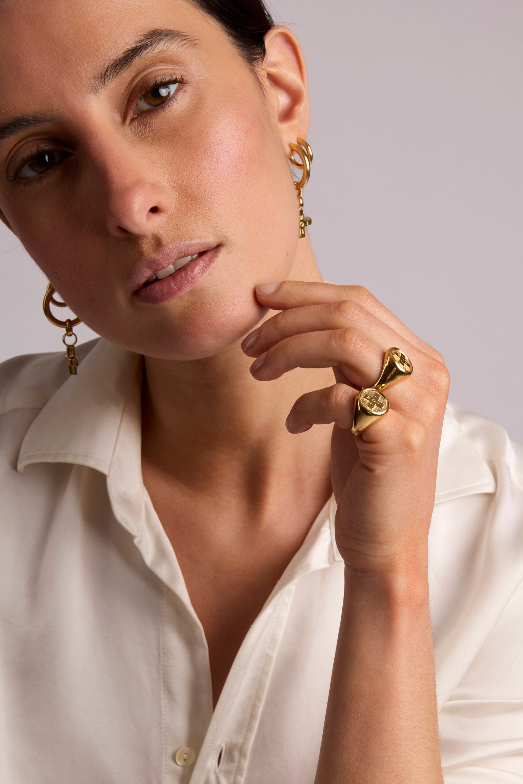 Woman wearing gold earrings and a ring, with a neutral background
