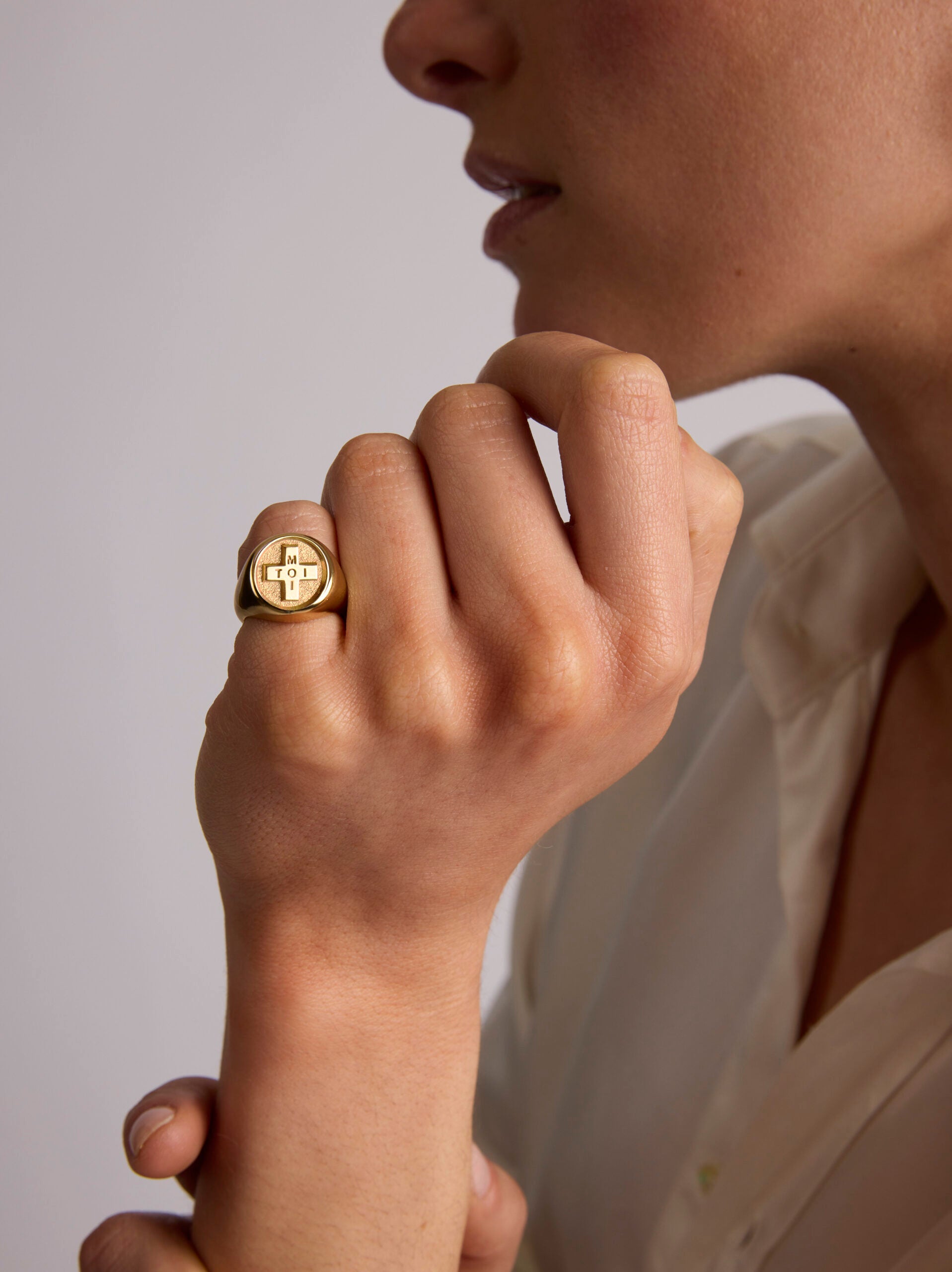 Close-up of a person wearing a gold ring with a heart design on a neutral background