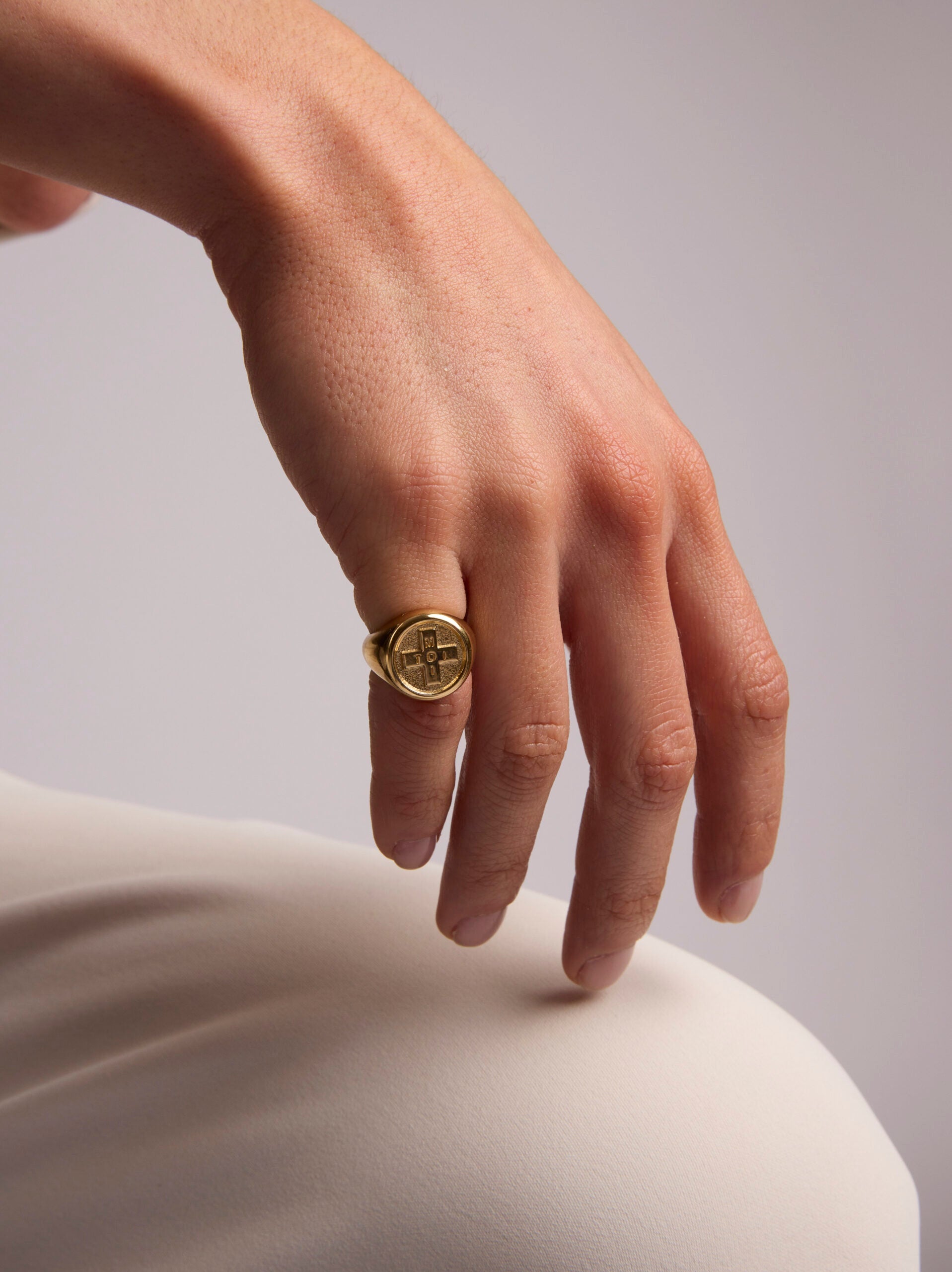 Hand wearing a gold ring on a neutral background
