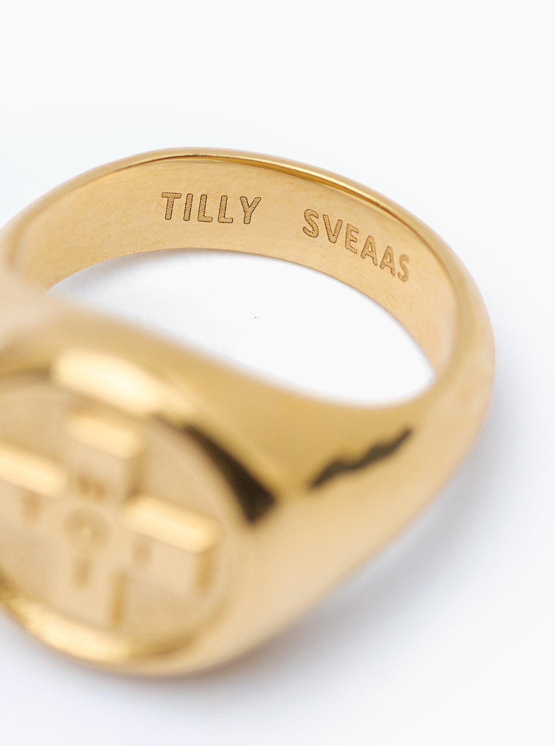 Gold ring with 'TILLY SVEAAS' engraving on a white background