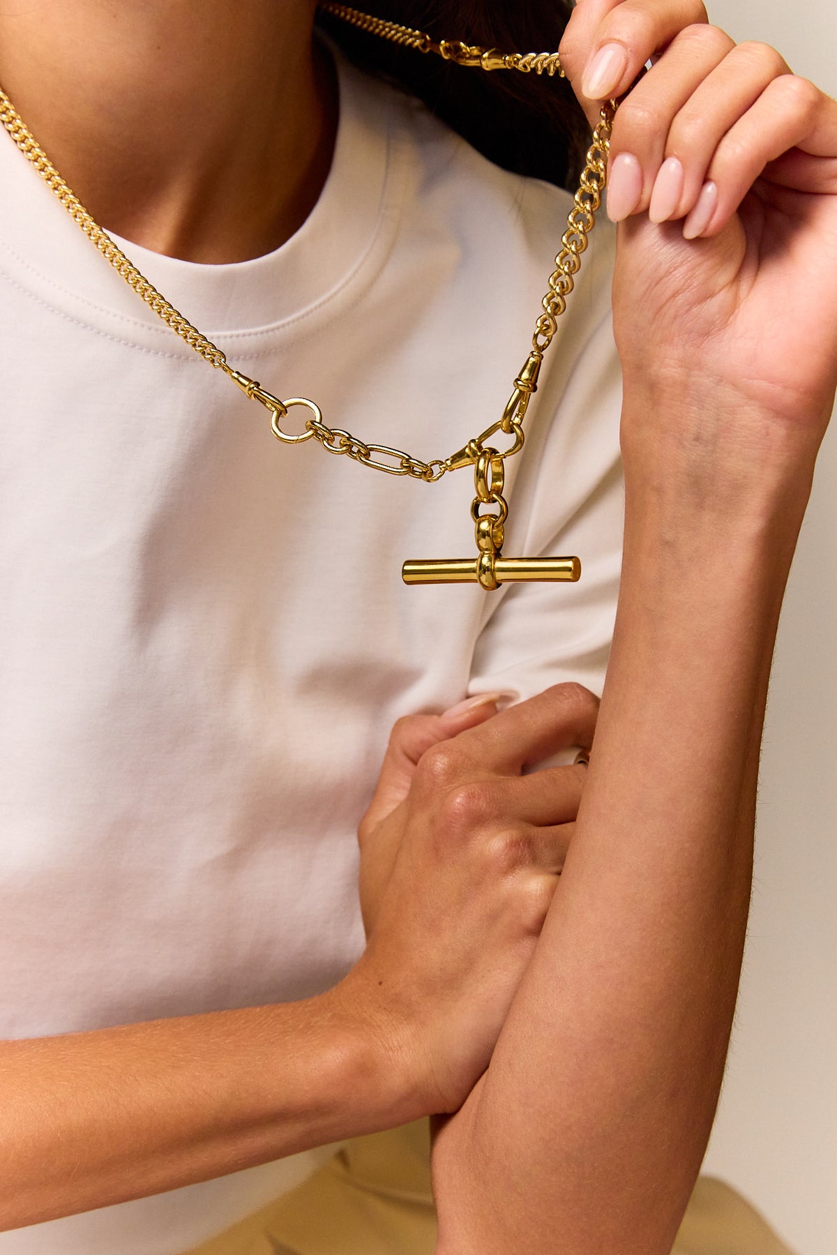 Close-up of a gold-tone chain necklace with linked sections and a T-bar pendant