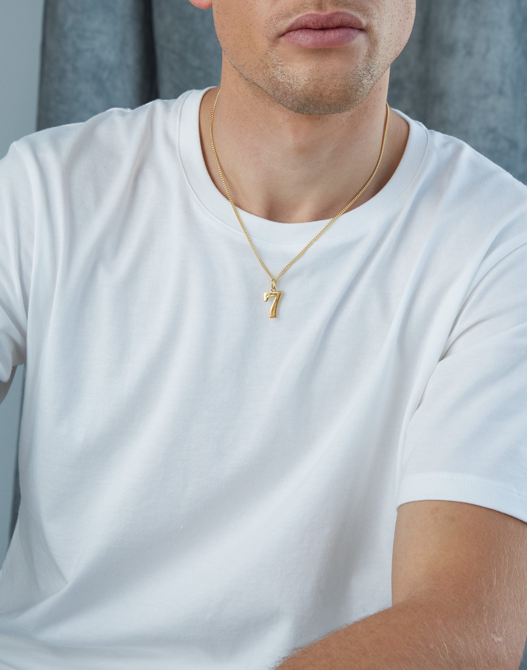 Man wearing a gold necklace with a small pendant on a plain background - Tilly Sveaas